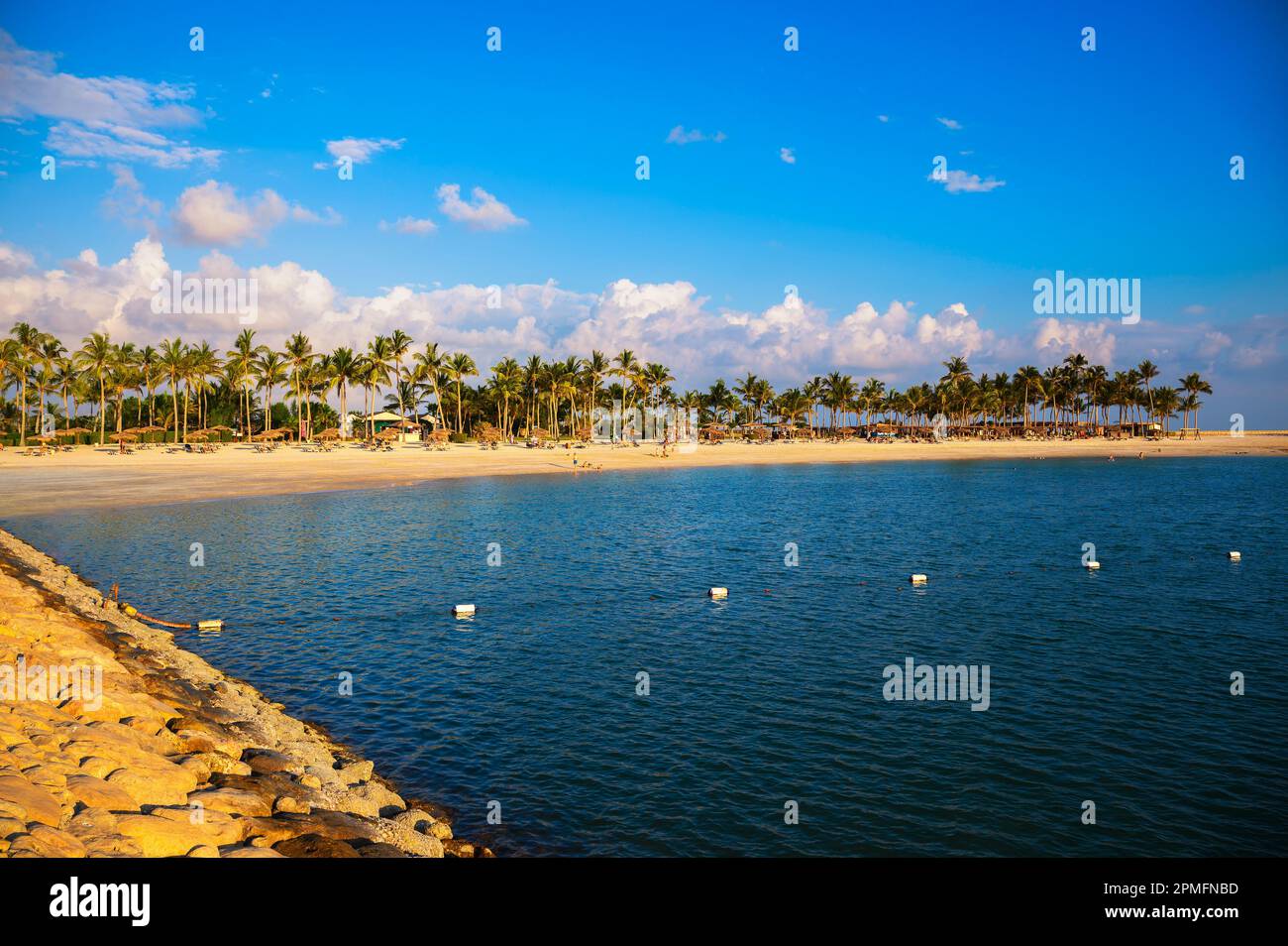 Sonniger Strand mit Palmen, Sonnenschirmen und Touristen in Salalah, Oman Stockfoto