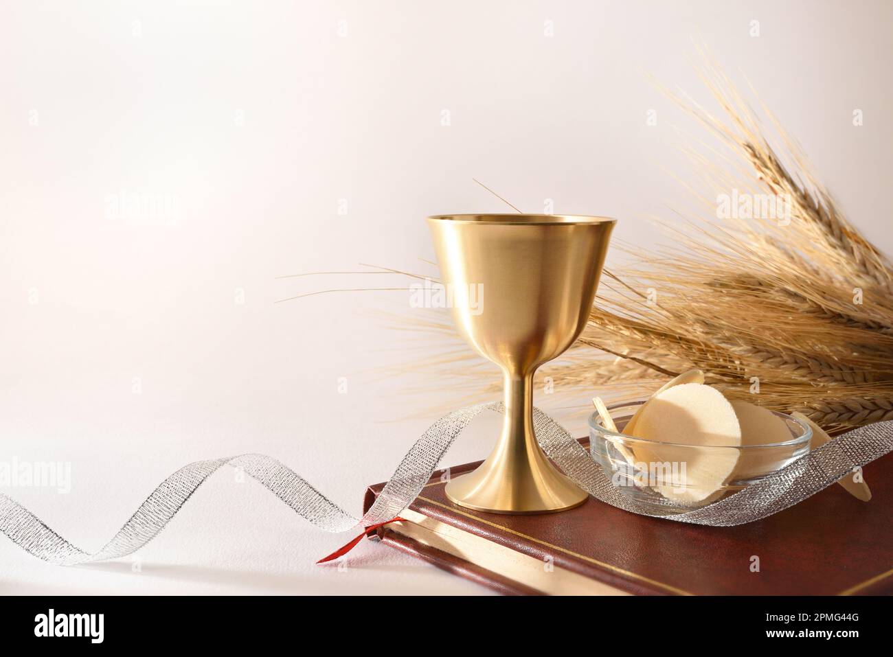 Eine Tasse Wein und Gastgeber in der bibel für eucharist auf einem weißen Tisch mit silbernem Band und dekorativen Weizenohren und einem weißen isolierten Hintergrund. Vorderansicht. Stockfoto