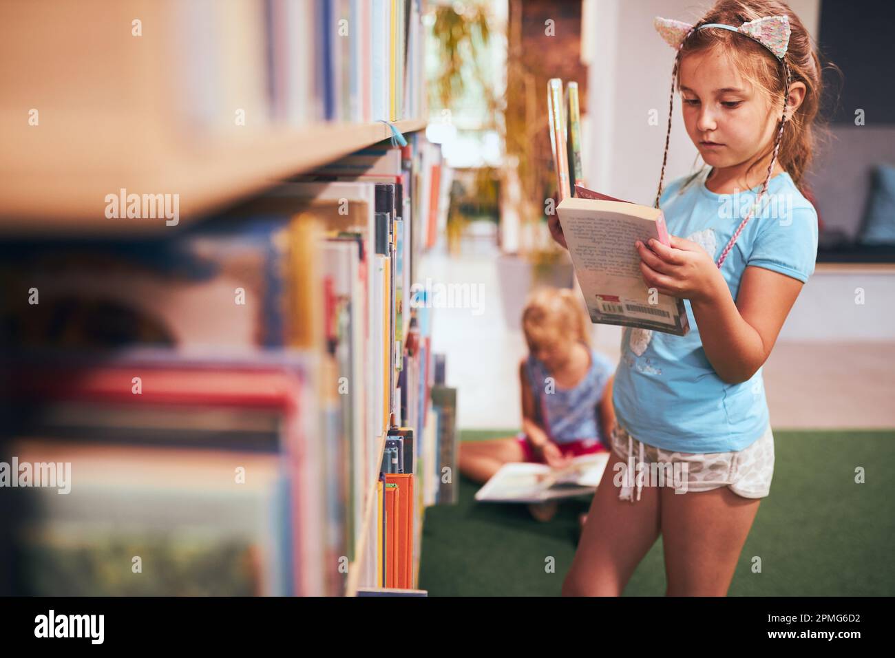 Schulmädchen, die ein Buch zum Lesen in der Schulbibliothek suchen. Schüler, die Bücher zum Lesen aussuchen. Aus Büchern lernen. Zurück in die Schule. Grundschule Stockfoto