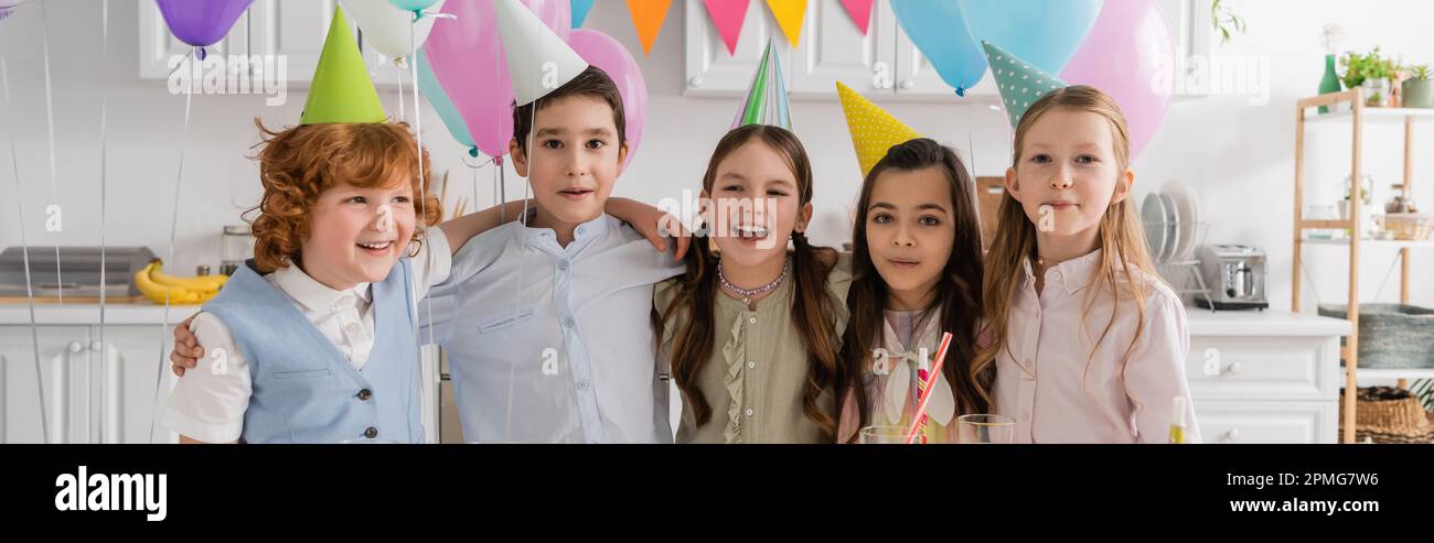 Positive Gruppe von Kindern, die neben dem Kuchen ein Happy Birthday Lied singen, mit Kerzen und Ballons, Banner, Stockbild Stockfoto