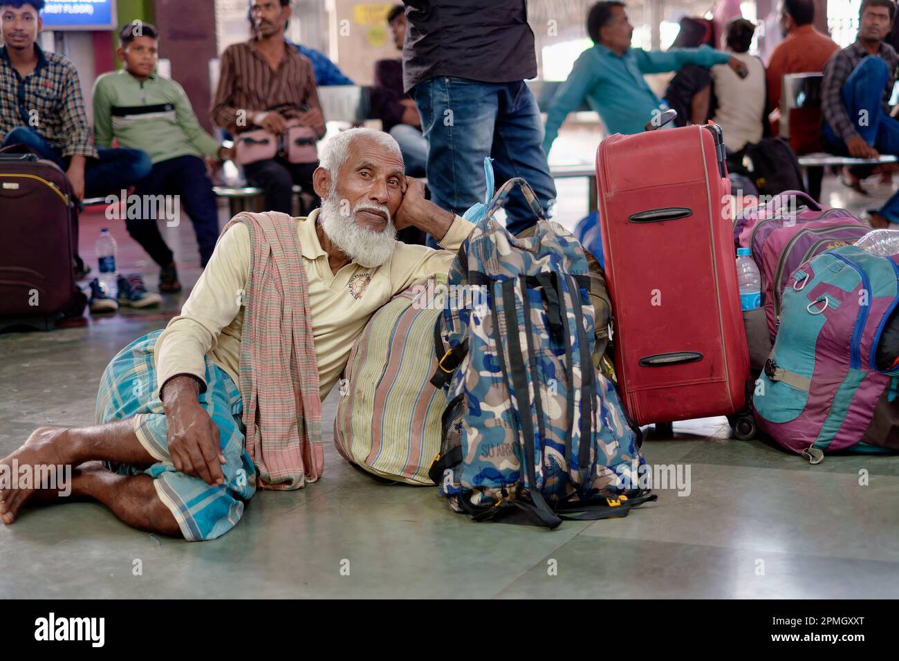 Ein bärtiger muslimischer Mann aus Kalkutta, der sich neben seinem Gepäck entspannt, während er auf seinen Zug wartet; Chhatrapati Shivaji Maharaj Terminus in Mumbai, Indien Stockfoto