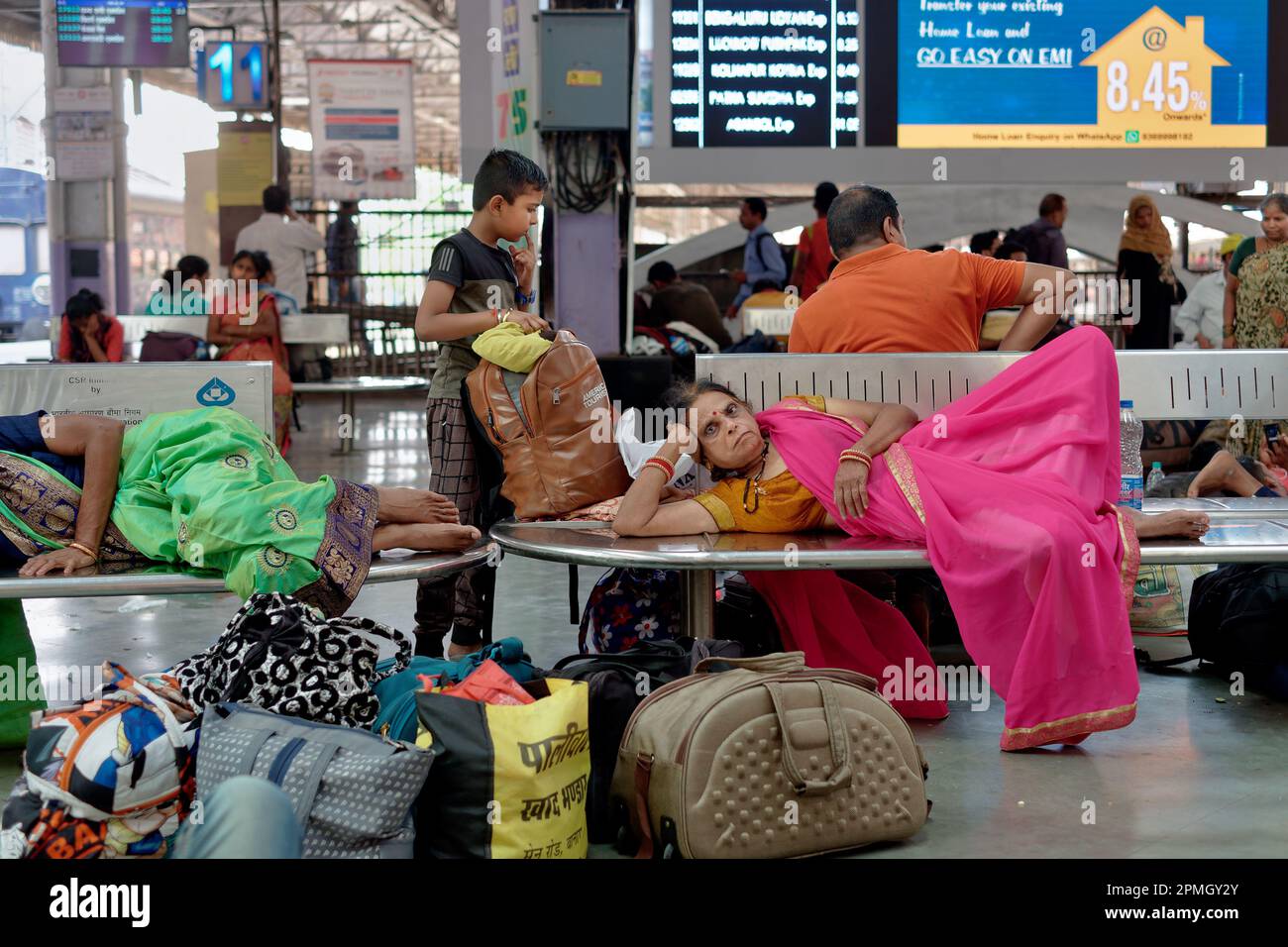 Eine Sari-bekleidete Zugfahrerin am Chhatrapati Shivaji Maharaj Terminus in Mumbai, Indien, entspannt sich auf einer Bank, während sie auf ihren Zug wartet Stockfoto