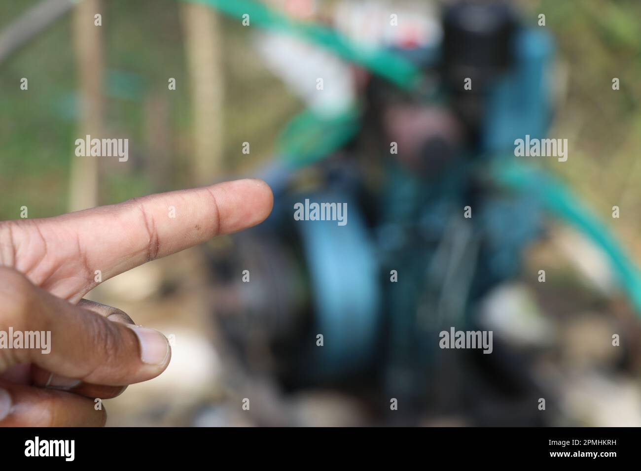 Die Hand zeigt auf eine Zentrifugalwasserpumpe, die von einem Dieselmotor auf unscharfem Hintergrund betrieben wird Stockfoto