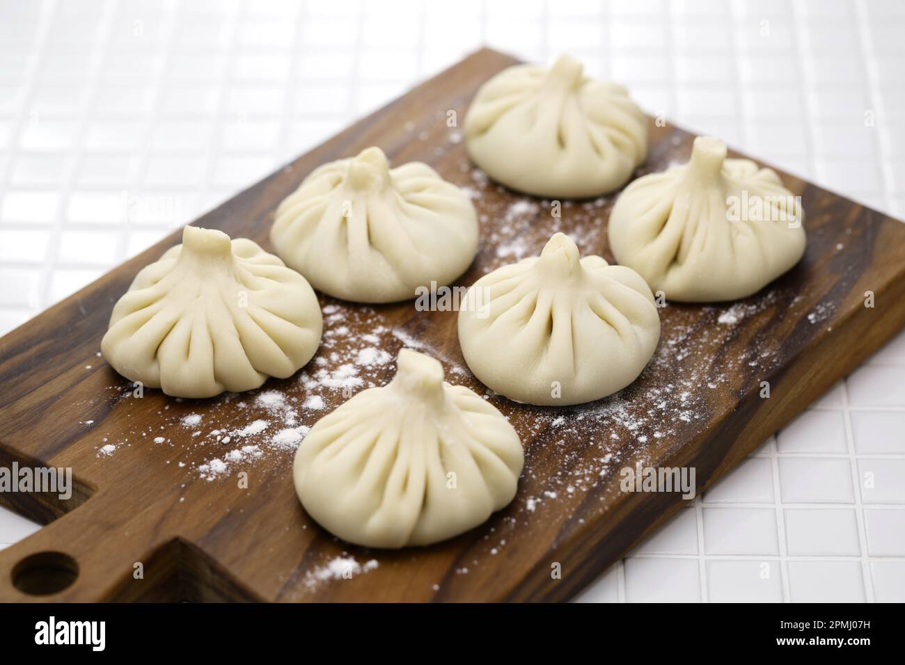 Hausgemachtes ungekochtes Khinkali auf einem Schneidebrett für Olivenholz, georgische Knödel Stockfoto