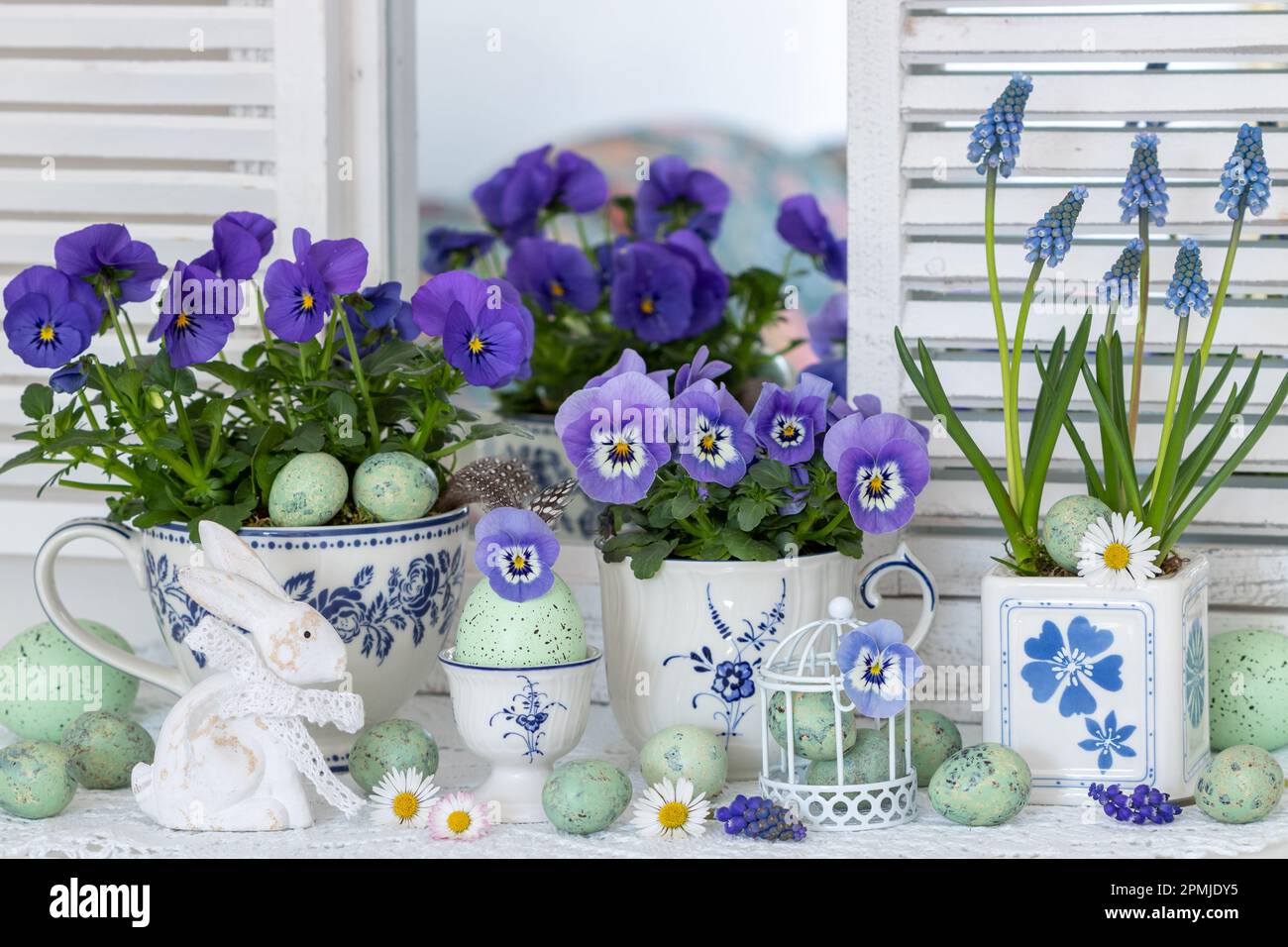 osterarrangement mit blauen Frühlingsblumen in Bechern, ostereiern und osterhasen Stockfoto