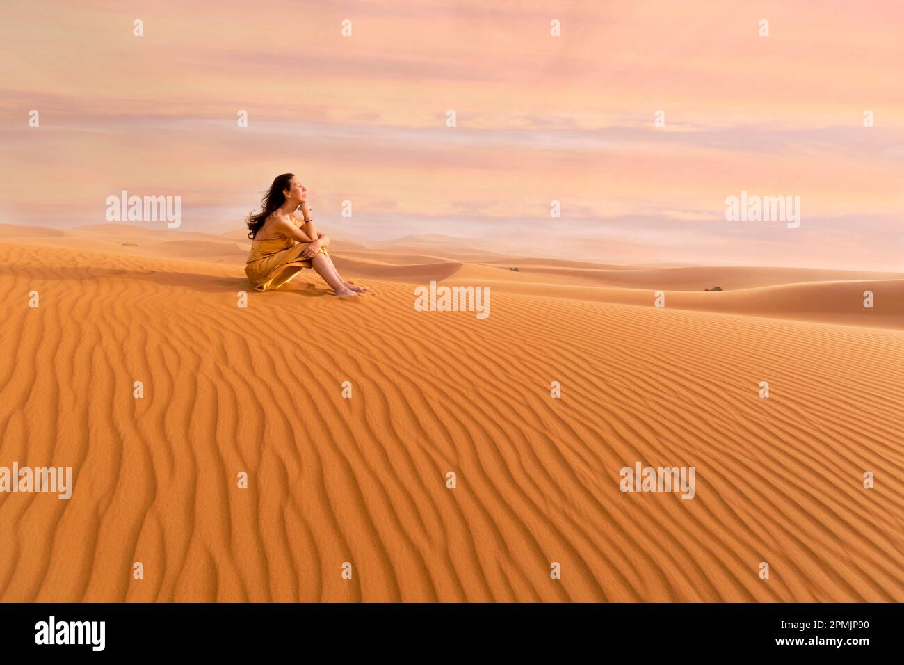 Eine Frau in gelbem Kleid, die mit dem Wind in der Wüste II spielt Stockfoto