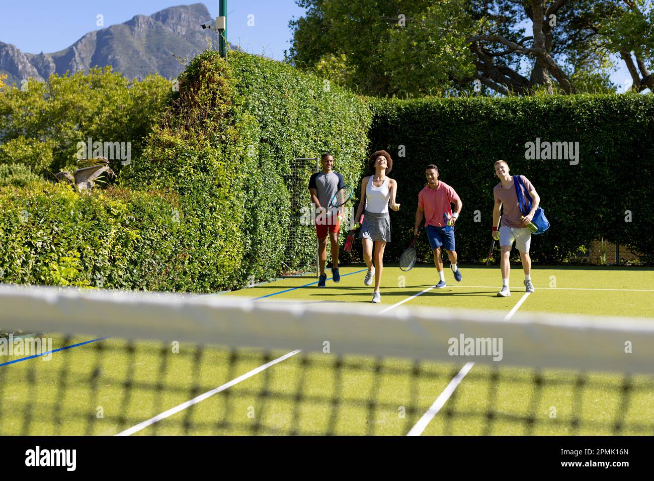 Glückliche, vielfältige Gruppe von Freunden, die zusammen auf dem Tennisplatz ankommen Stockfoto