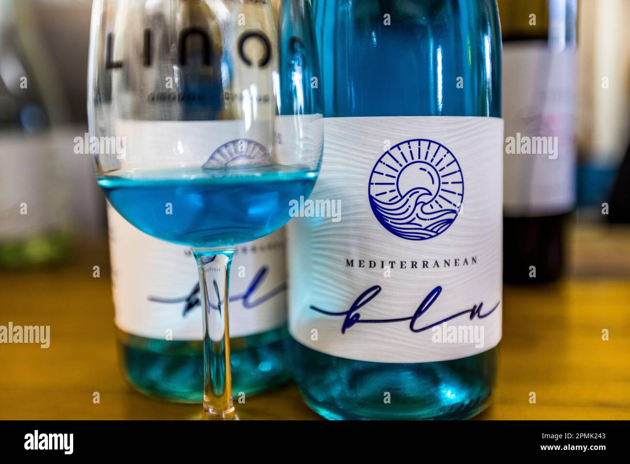 Ein Glas und eine Flasche "Mediterranean Blu" stehen auf einem Tisch im Linos-Weingut (Ktima Herodotou) in Omodos, Republik Zypern. Das Rezept für den blauen Aperitifwein ist das Geheimnis des Weinguts. Seine Farbe entwickelt sich natürlich, wenn Weißwein kurz mit den Schalen roter Trauben in Kontakt kommt. Seit 1825 von der Familie Herodotou geführt, brachte das Weingut den Wein 2020 auf den Markt und wurde damit erst das sechste Weingut weltweit, das einen blauen Wein herstellt, der aus der einheimischen weißen Xynisteri-Traube gemacht wird. Stockfoto
