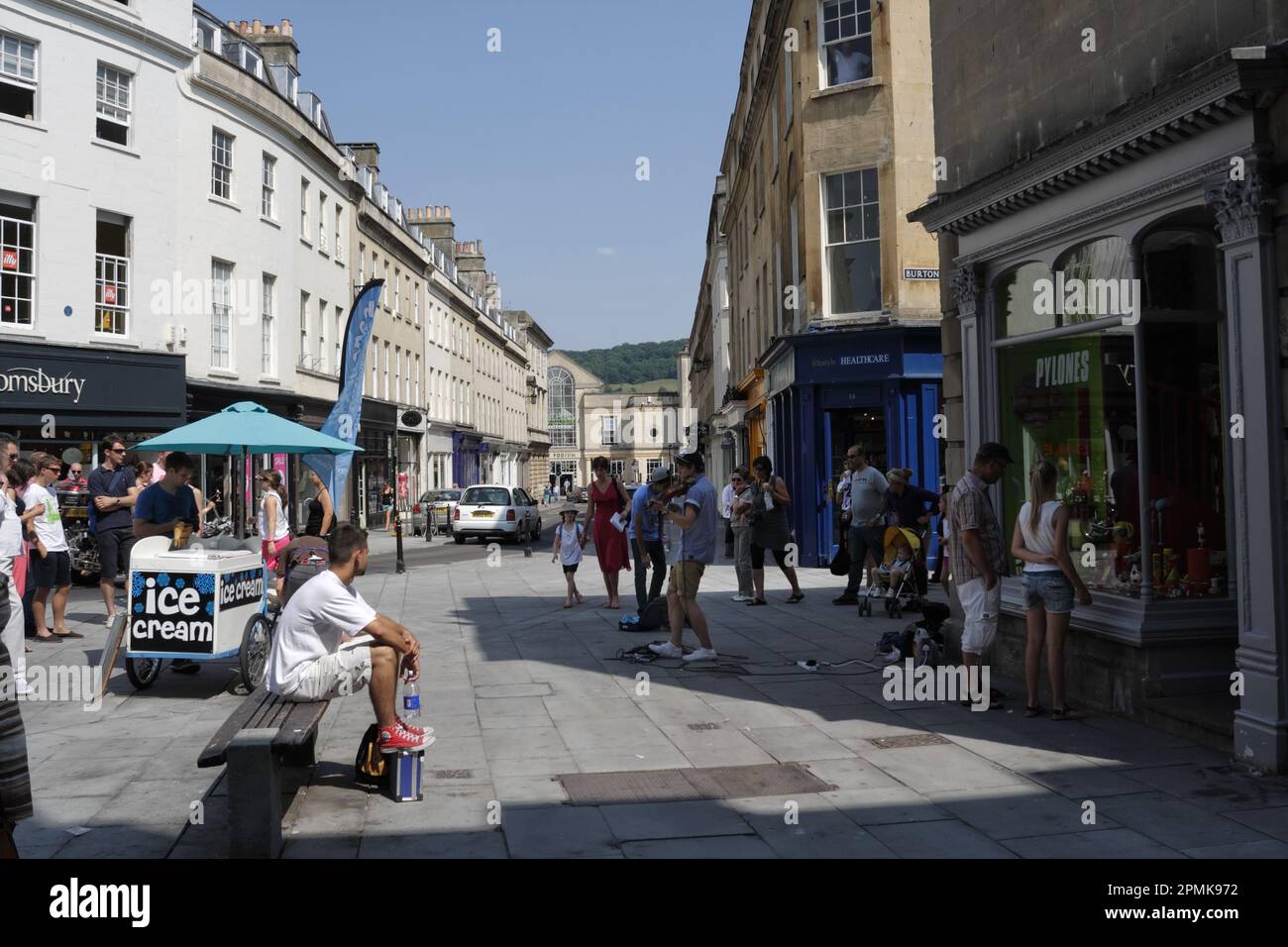 Leute, die einen Straßenmusiker beim Spielen in Bath City Center England beobachten. Englische Stadtmitte, Straßenszene im Schaufenster der britischen Stadt Stockfoto