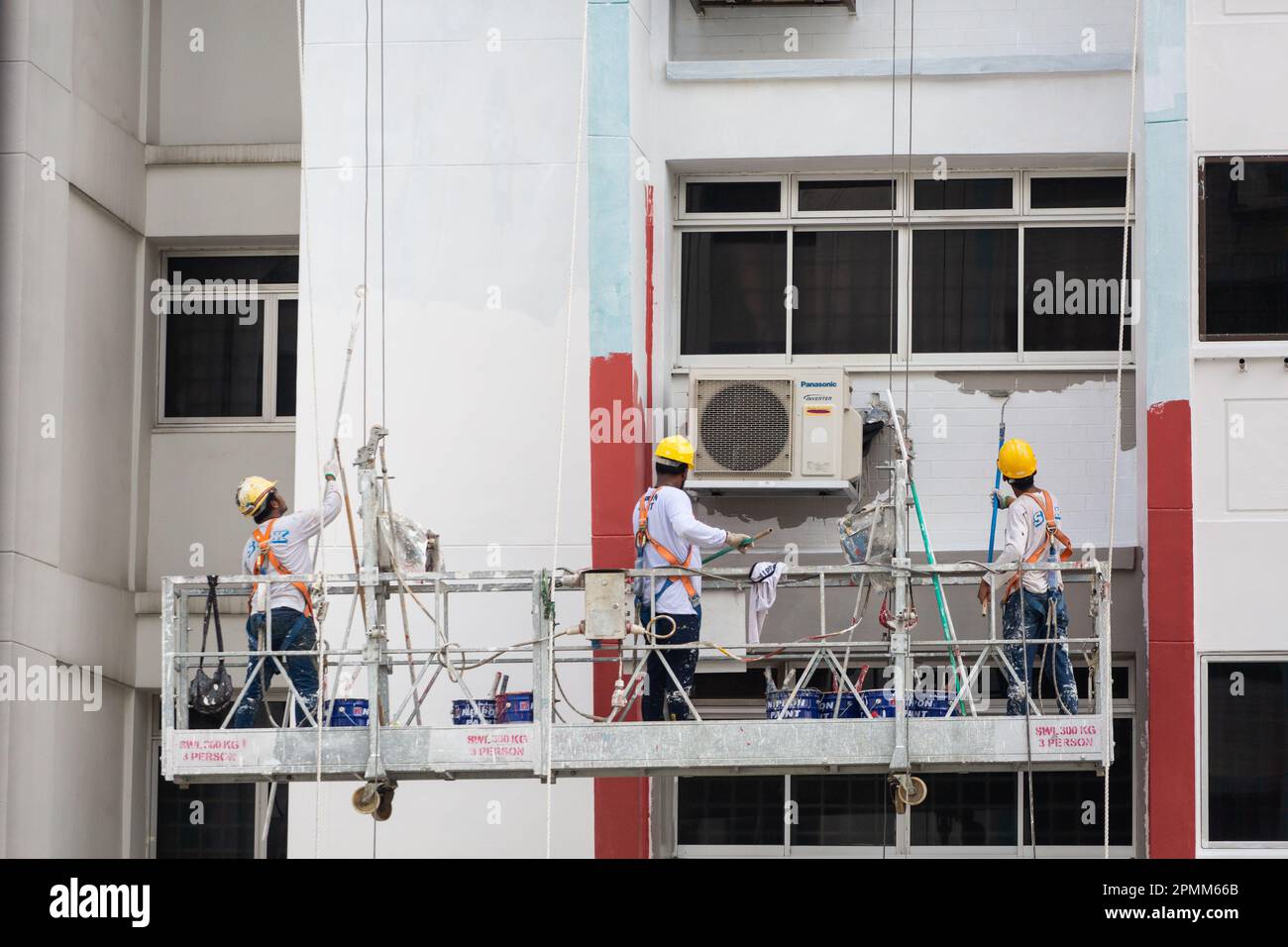 Nahaufnahme eines Gerüstaufzugs mit 3 Malern streichen eine frische Lackschicht auf die Gehäuseaußenseite, um ein frisches Aussehen zu verleihen. Singapur. Stockfoto