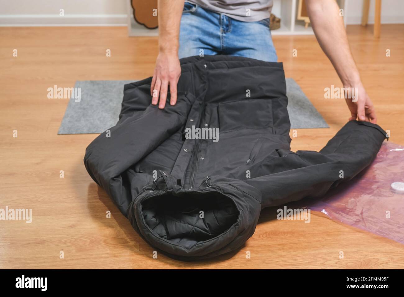 Ein Mann faltet Winterjacken und legt sie in einen Staubsauger, um sie  saisonal im Schrank aufzubewahren. Platzsparend und schonende Aufbewahrung  von Kleidung. Organisation Stockfotografie - Alamy