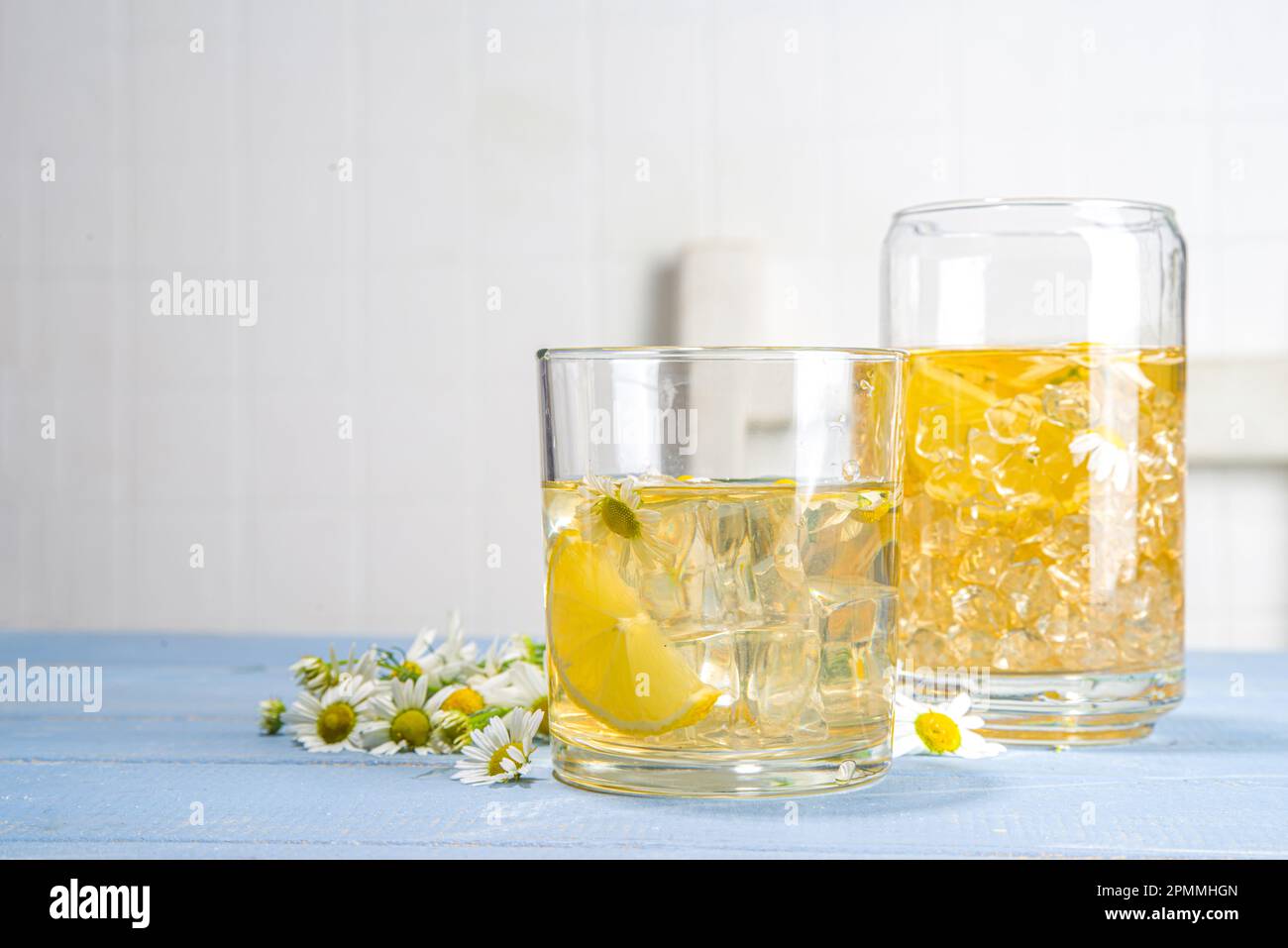 Pflanzliches organisches kaltes Getränk. Infundiert mit Blumenwasser. Iced Daisy Kamille Tee oder Limonade mit Zitronenscheibe und Eiswürfeln, in zwei verschiedenen Gläsern, blau w Stockfoto