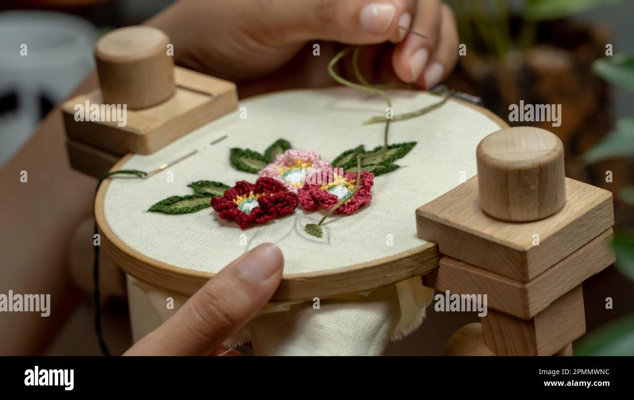 Frauenhände, die eine Blume auf einen Holzkorb sticken. Stockfoto