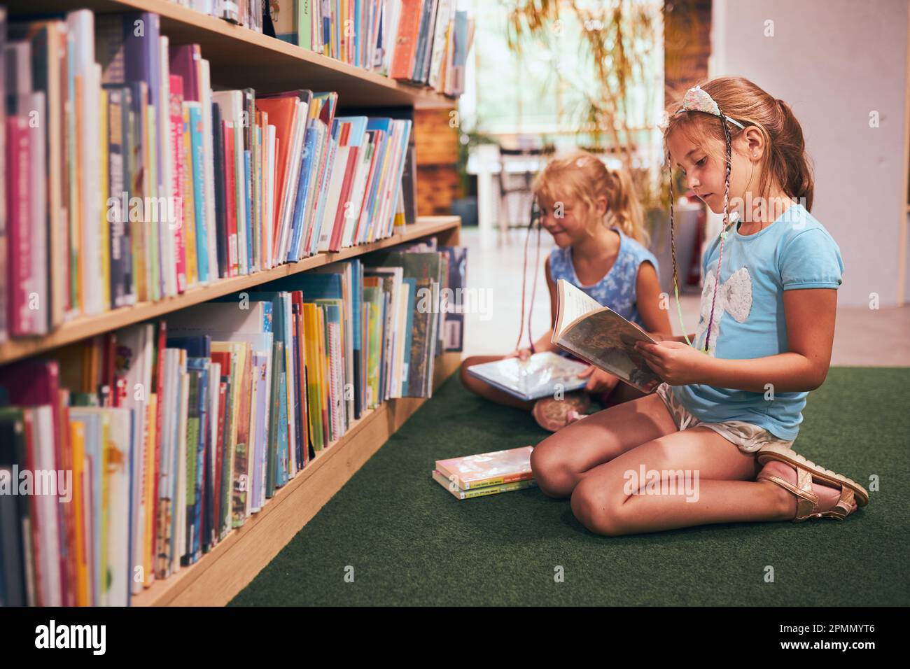 Schulmädchen, die ein Buch zum Lesen in der Schulbibliothek suchen. Schüler, die Bücher zum Lesen aussuchen. Aus Büchern lernen. Zurück in die Schule. Grundschule Stockfoto