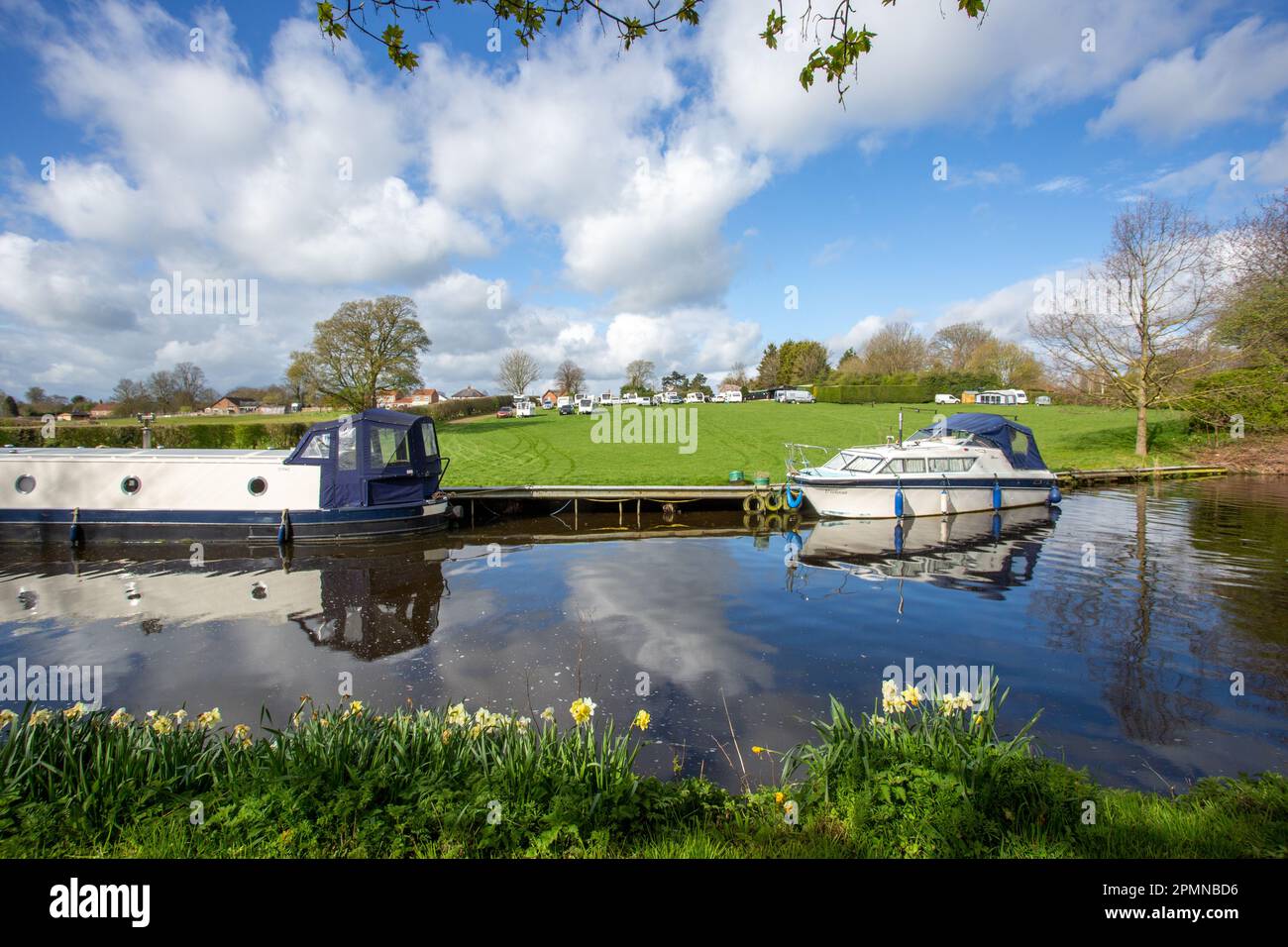 Kanal-Schmalschiff und Vergnügungsboot auf dem Ripon-Kanal, North Yorkshire im Frühling, mit Narzissen, die auf dem Schleppweg wachsen Stockfoto Kanal-Schmalschiff und Vergnügungsboot auf dem Ripon-Kanal, North Yorkshire im Frühling, mit Narzissen, die auf dem Schleppweg wachsen Stockfoto