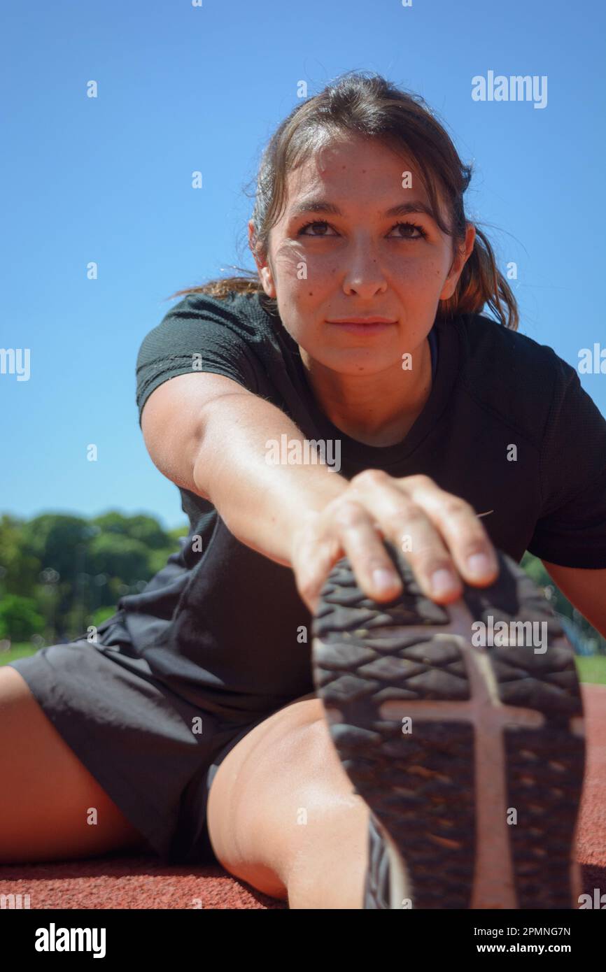 Nahaufnahme einer jungen lateinamerikanischen argentinierin in schwarzer Sportbekleidung, konzentriert sich auf dem Boden, mit der Hand auf der Fußspitze, senkrecht Stockfoto