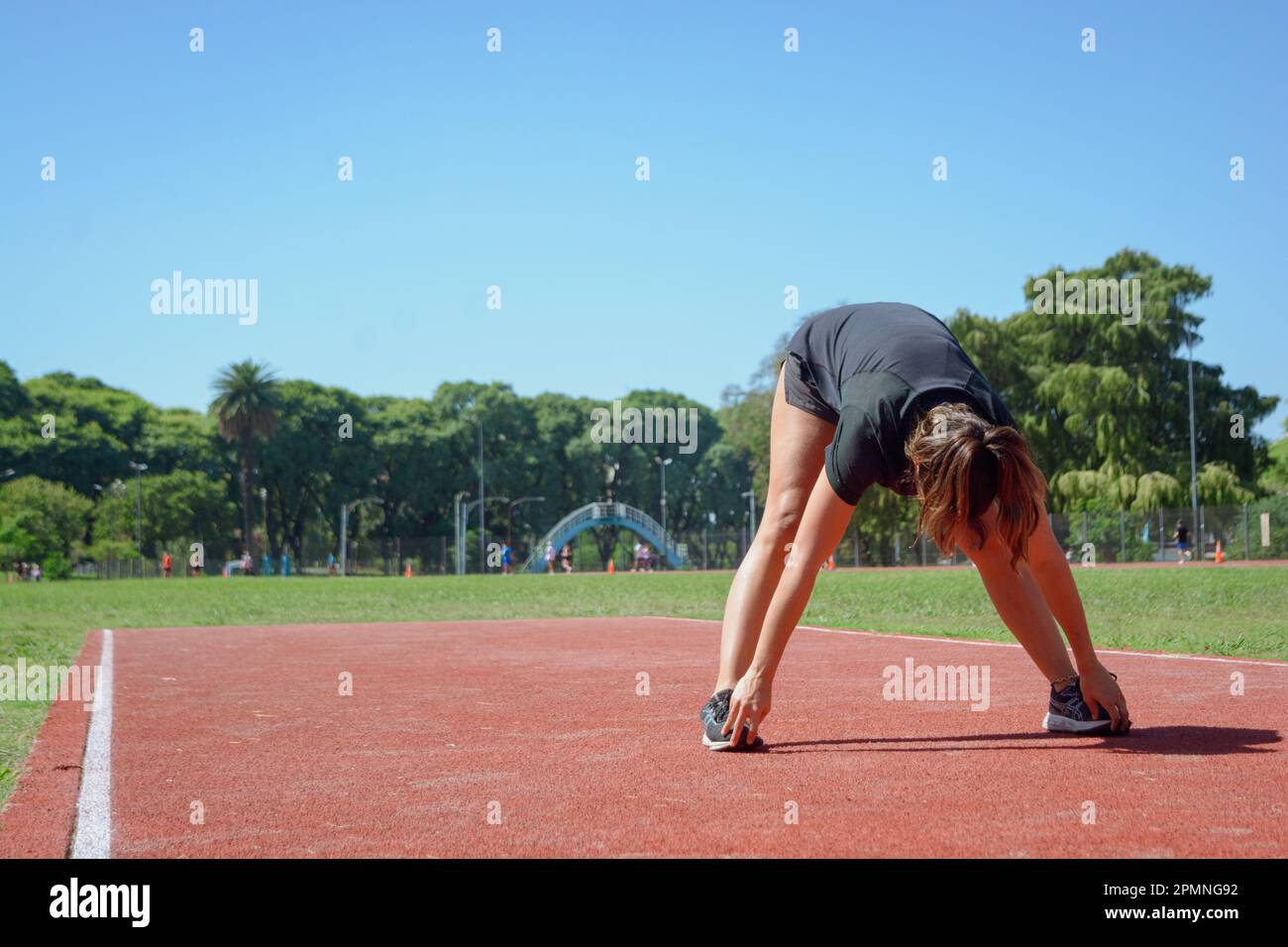 Junge Latina-Frau argentinischer ethnischer Herkunft, die sich auf der Laufbahn ausstreckt, steht und sich nach vorn lehnt und ihre Füße mit ihren Händen berührt, trainiert g Stockfoto