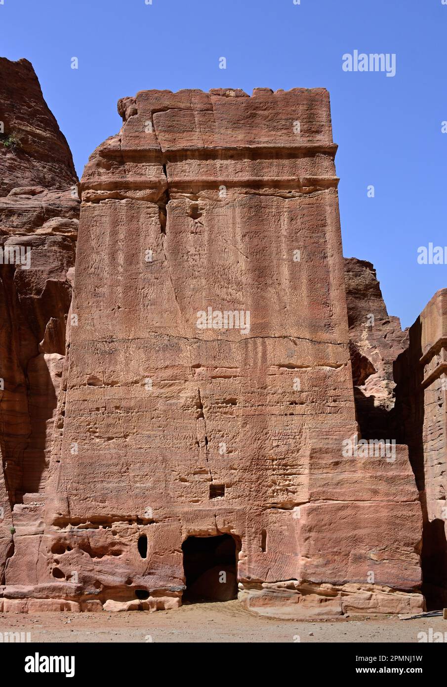 Monumentale in den Fels gehauene Fassade des Palastgrabes entlang der zerklüfteten Sandsteinklippen des Royal Tombs unter einem klaren blauen Himmel Petra, Jordanien Stockfoto