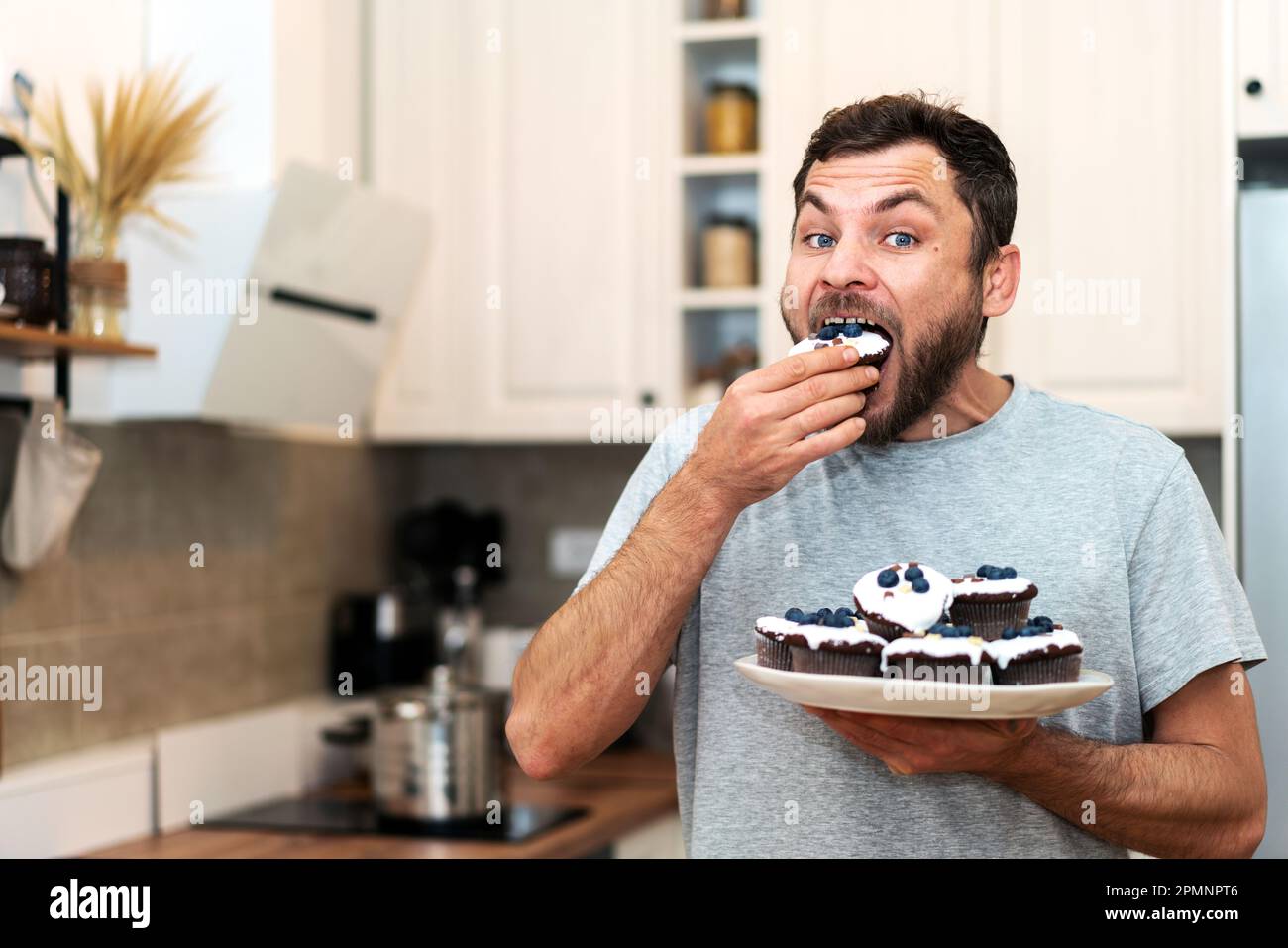 Hungriger Mann, der hausgemachte Cupcakes in der Küche isst. Stockfoto