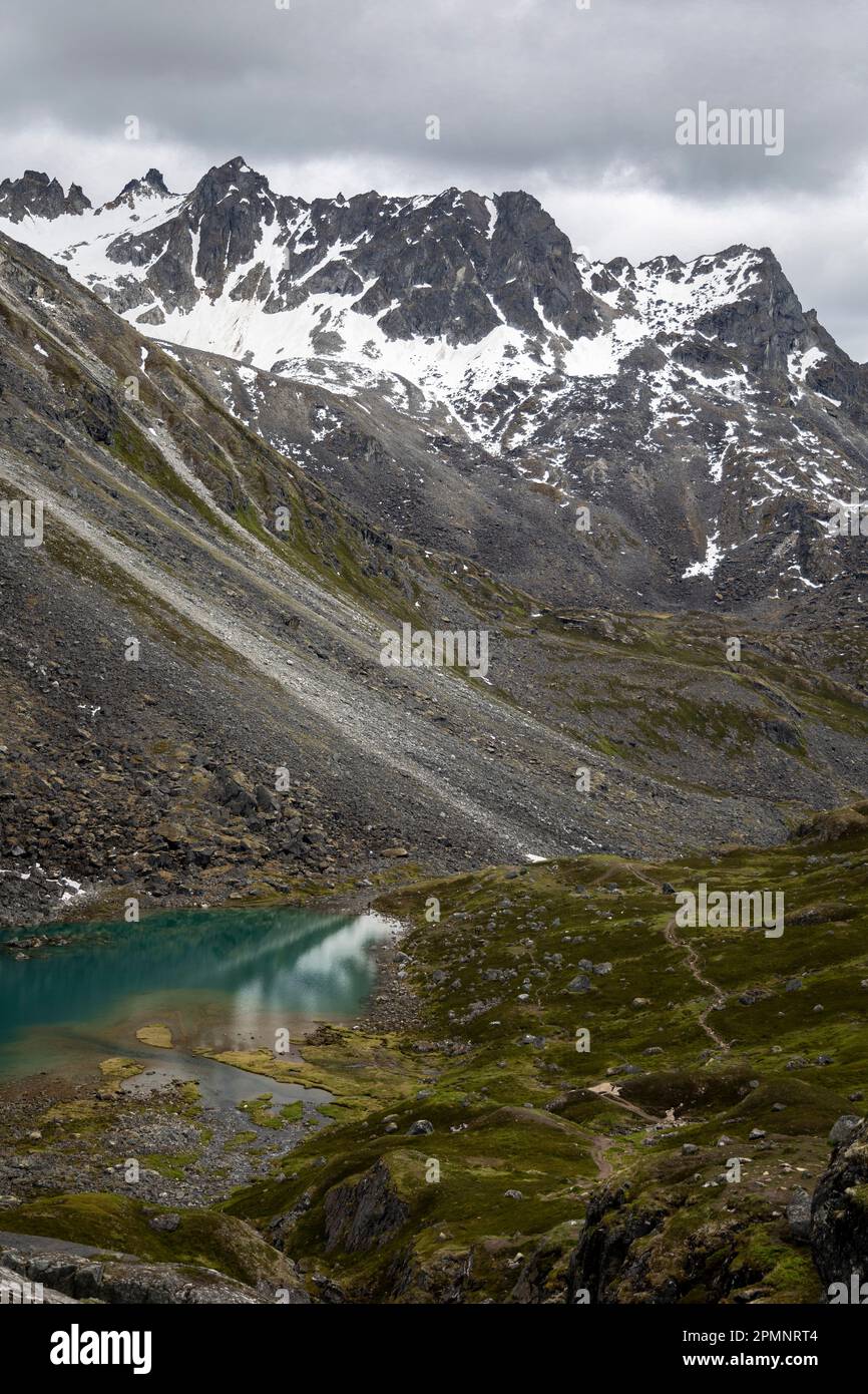 Granitgipfel am Hatcher Pass unter einem grauen, wolkigen Himmel mit dem dunklen türkisfarbenen Wasser der Reed Lakes in der Nähe der Independence Mine Stockfoto