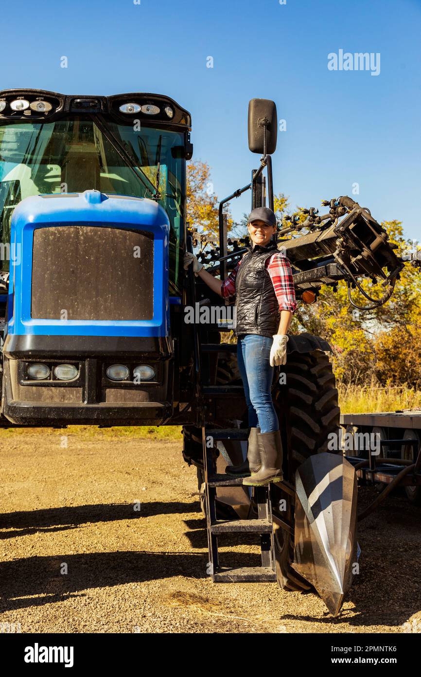 Porträt einer Landwirtin, die auf den Stufen eines Traktors mit Sämaschinen steht; Alcomdale, Alberta, Kanada Stockfoto