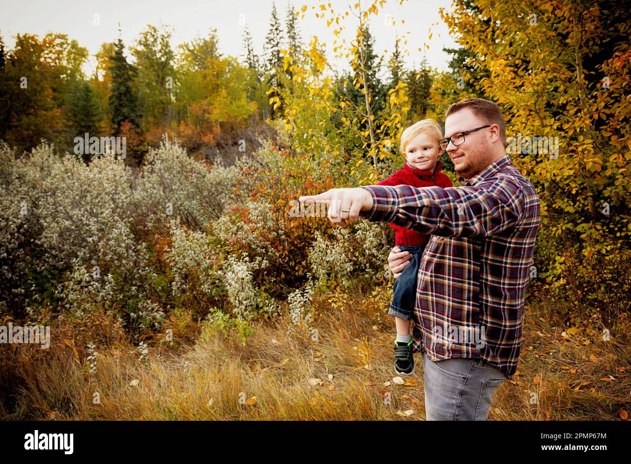 Porträt eines Vaters mit seinem jungen Sohn, der im Herbst in einem Park in Edmonton, Alberta, Kanada, die Natur erkundet Stockfoto