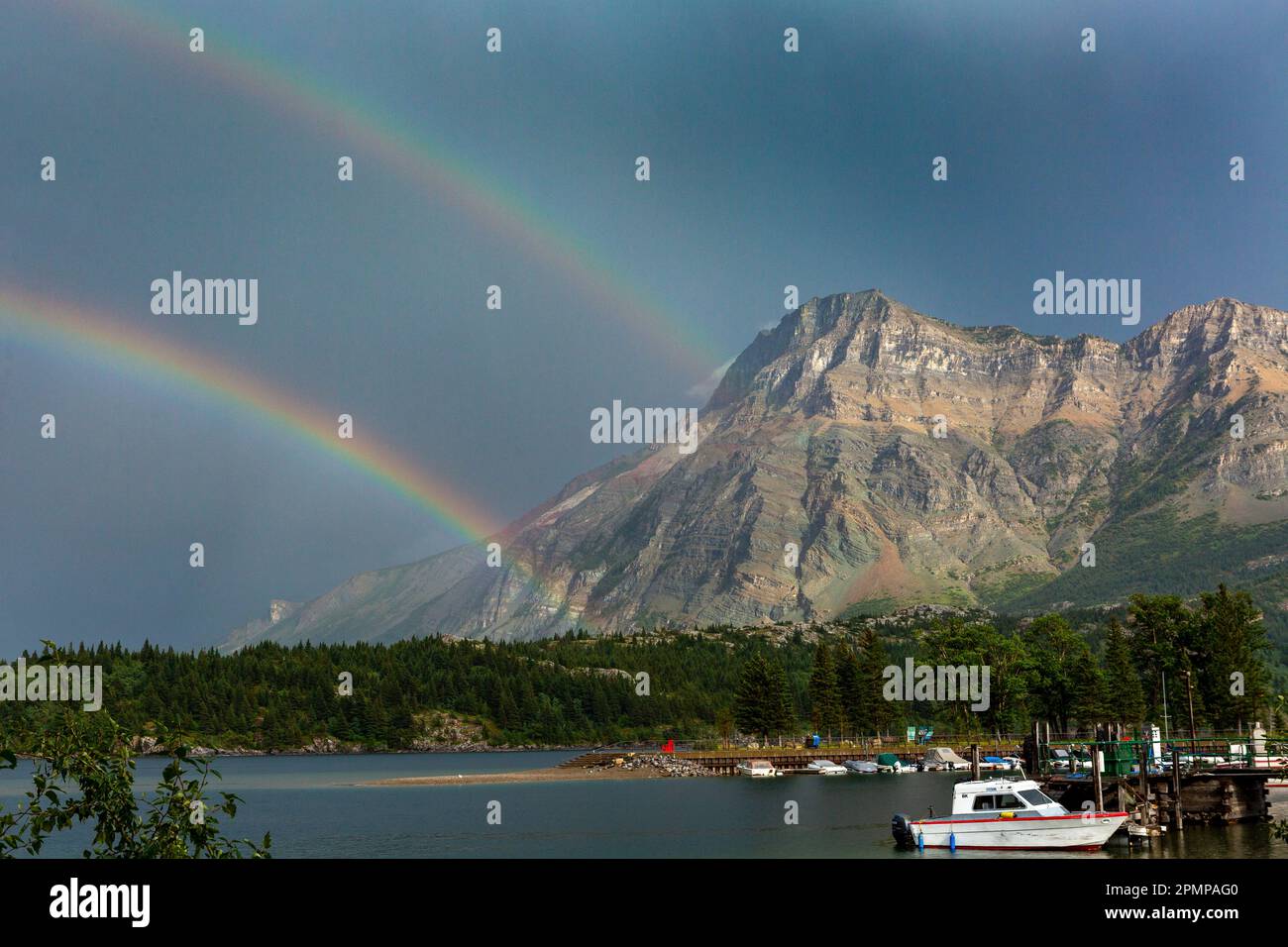 Doppelter Regenbogen mit Bergen am Seeufer und dunkelblauem Himmel im Waterton Lakes National Park in Waterton, Alberta, Kanada Stockfoto