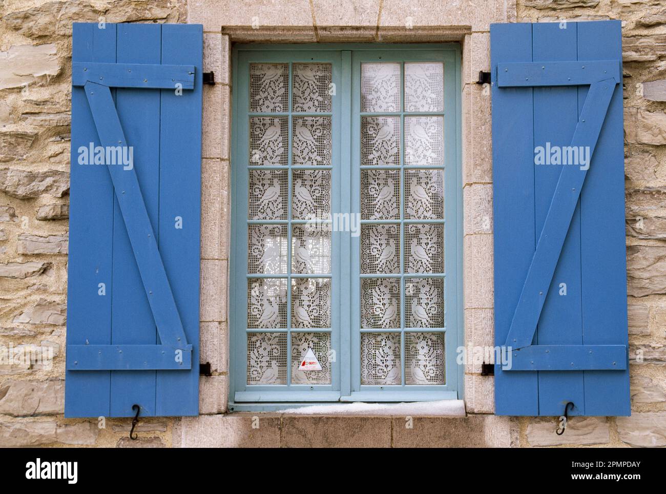 Spitzenvorhang mit Vögeln in einem Fenster mit blauen Fensterläden; Cap-Chat, Gaspe, Quebec, Kanada Stockfoto