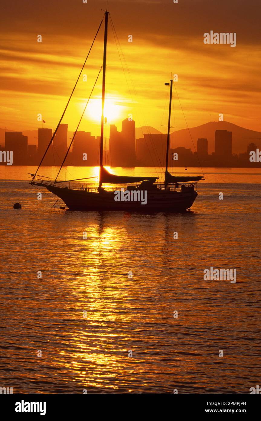 Silhouettensegelboot bei Sonnenaufgang mit Skyline von San Diego in der Ferne, Kalifornien, USA; San Diego, Kalifornien, Vereinigte Staaten von Amerika Stockfoto