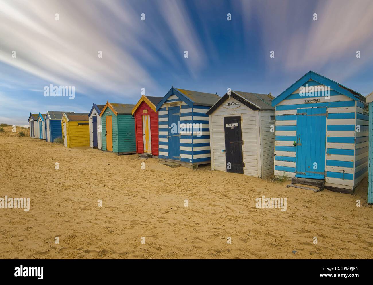 Der perfekte Strandtag - goldener Sand, wunderschöne, farbenfrohe Strandhütten und blauer Himmel in Southwold. Stockfoto