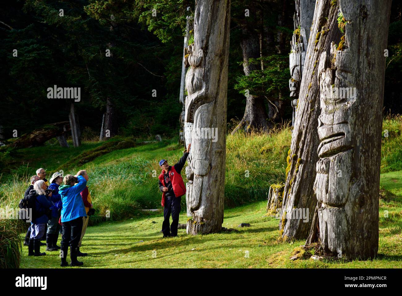 Touristen mit Reiseleiter sehen die Totempfähle in SGang Gwaay Llanagaay, Ninstints auf Englisch, einem verlassenen Ort in Haida auf Anthony Island Stockfoto