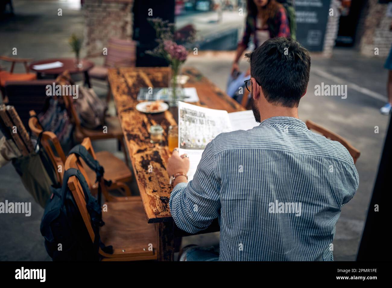 Rückansicht eines jungen Mannes, der im Café Zeitung liest und allein am Tisch sitzt. Moderne Café-Einrichtung. Stockfoto