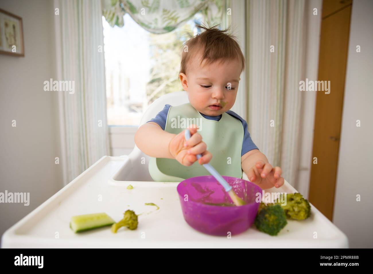 Süßes Baby isst erste feste Nahrung, Baby sitzt im Hochstuhl. Kind