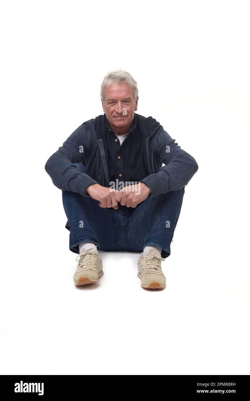 Vorderansicht eines Mannes, der mit gefalteten Beinen auf dem Boden sitzt und lächelt und auf die Kamera auf weißem Hintergrund blickt Stockfoto