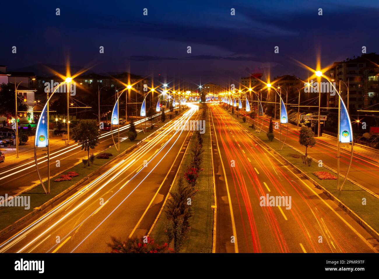 Der Verkehr fließt auf der Hauptstraße zur blauen Stunde im Zentrum von Malatya. Malatya Metropolitan Municipality Emblem an den Lichtmasten. Stockfoto