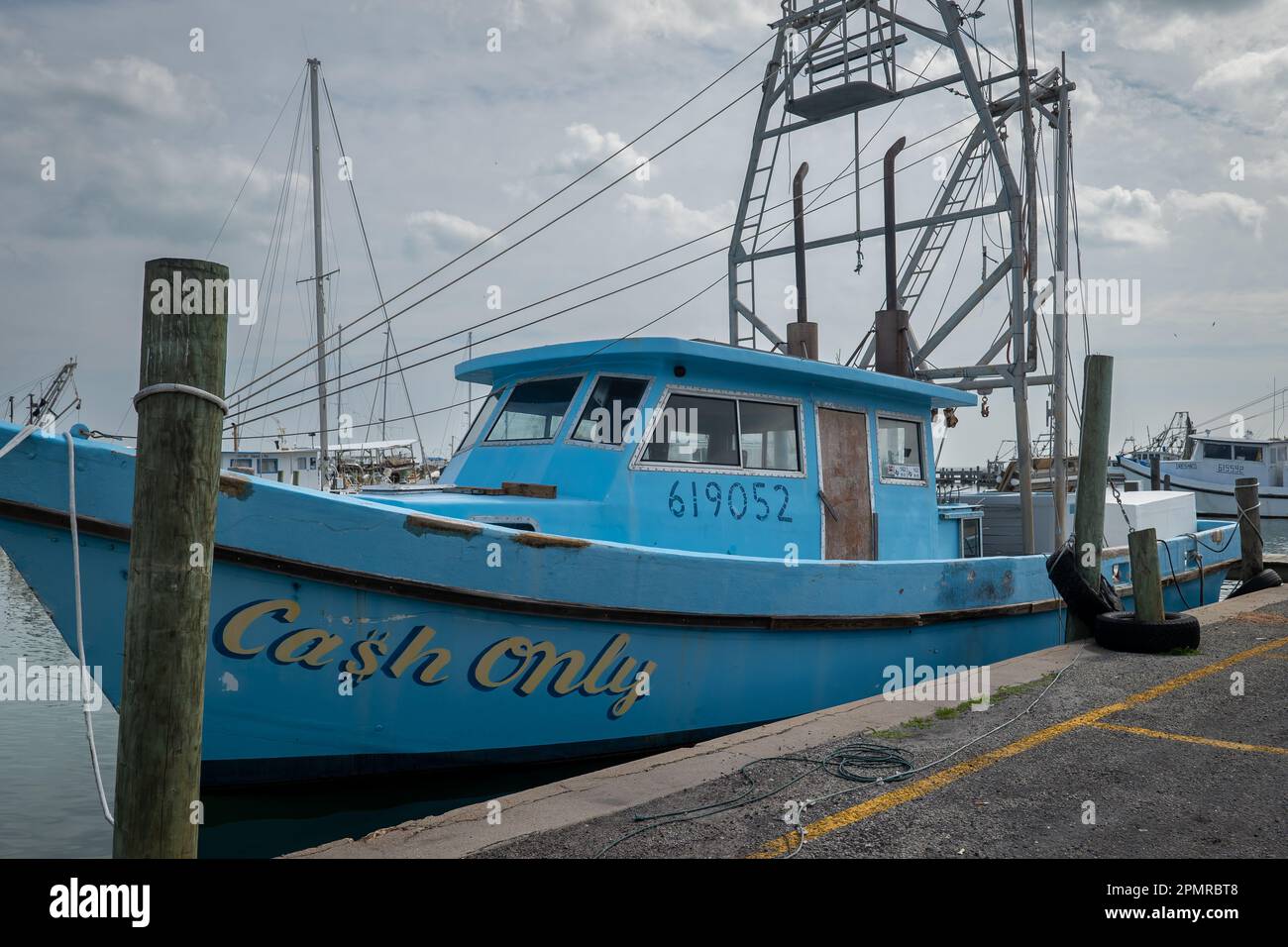 ROCKPORT, TX - 14. FEBRUAR 2023: Hafenseite eines blauen kommerziellen Fischerboots, NUR BARGELD, gebunden an Holzpfähle des Docks im Hafen auf Wolken Stockfoto