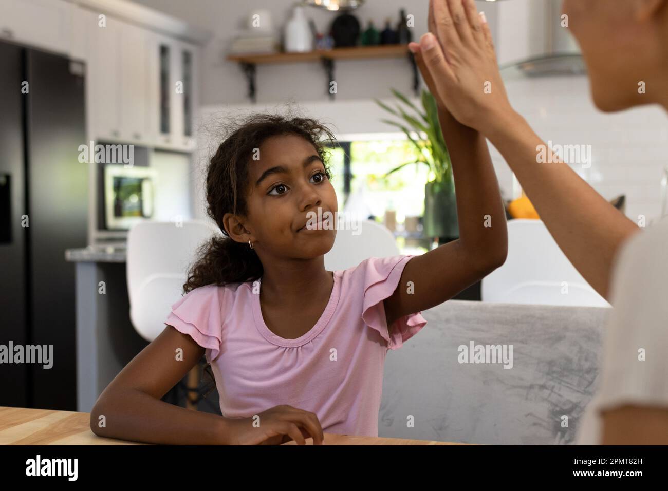 Rücksichtsvolle birassische Tochter, die mit ihrer Mutter an einem Tisch in der Küche sitzt Stockfoto