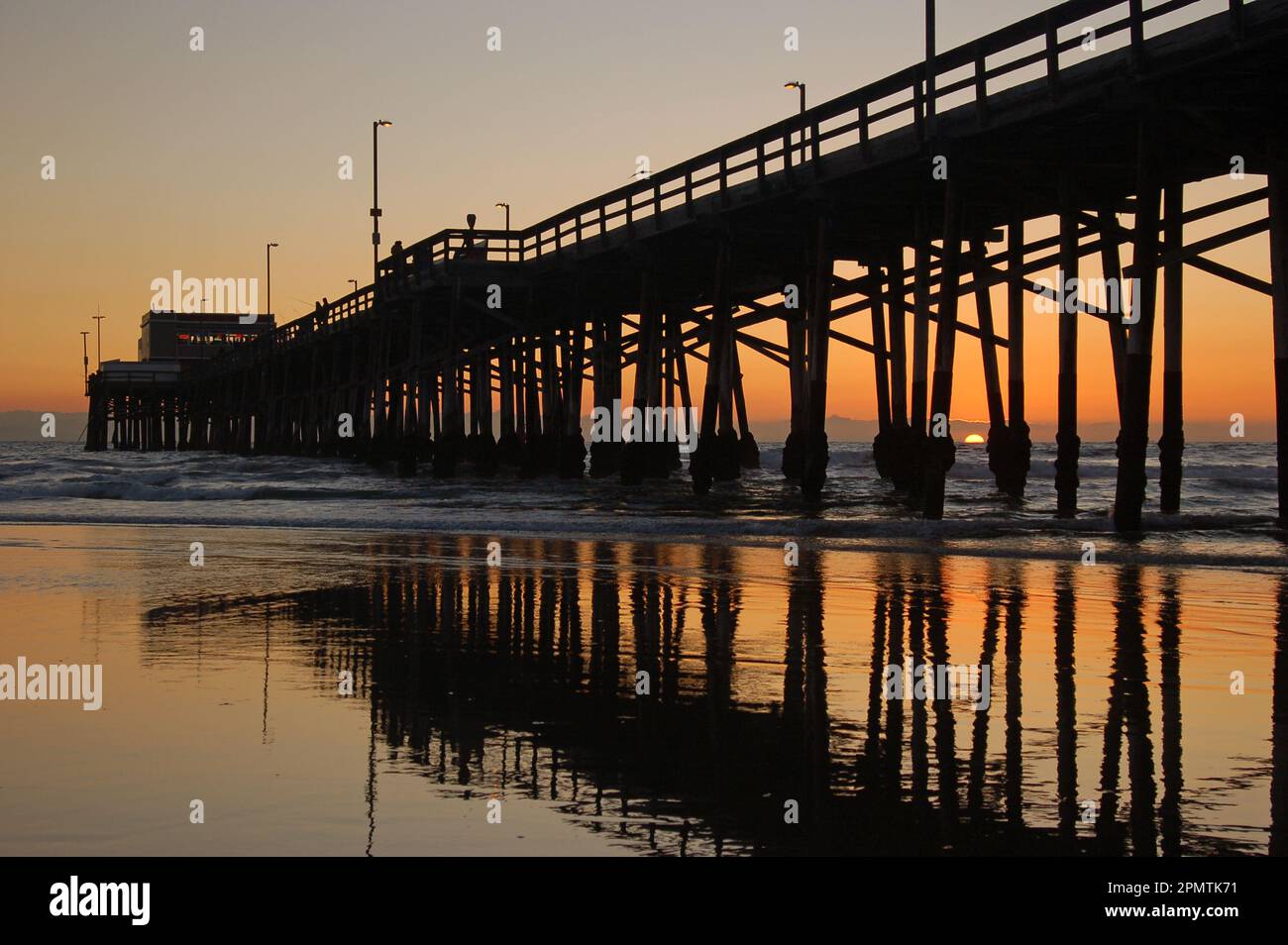 Die Sonne geht auf dem Pazifik und Newport Pier unter und spiegelt sich im Wasser der kalifornischen Küste Stockfoto