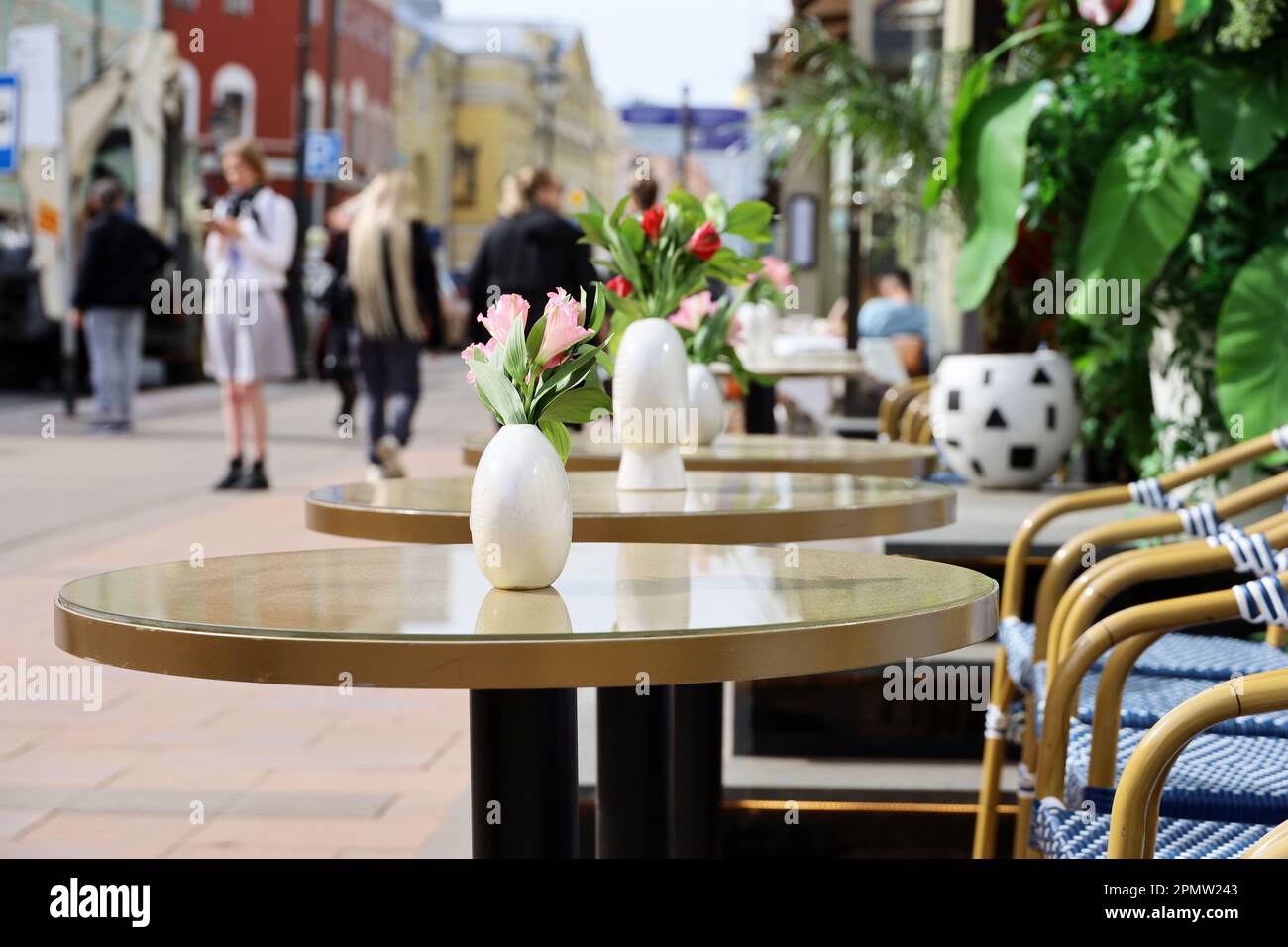 Straßencafe in der Stadt mit leeren Tischen draußen im Hintergrund für Spaziergänger. Blumen in Vasen auf runden Tischen an sonnigen Tagen Stockfoto