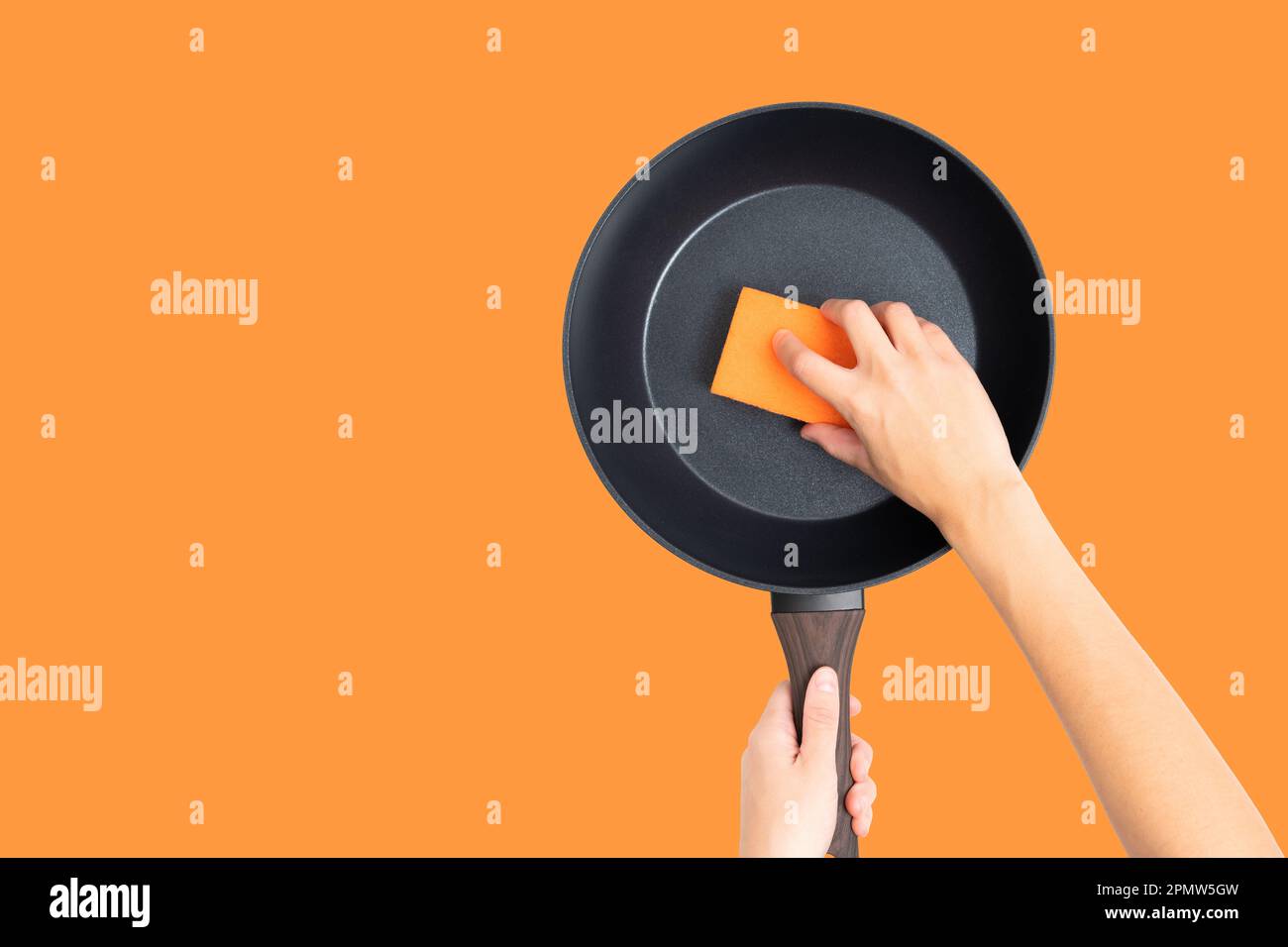 Schnittansicht mit weiblichen Händen, die eine Bratpfanne mit einem orangefarbenen Schwamm auf kräftigem orangefarbenen Hintergrund halten und reinigen. Hausarbeiten, Haushaltsarbeiten, KI Stockfoto