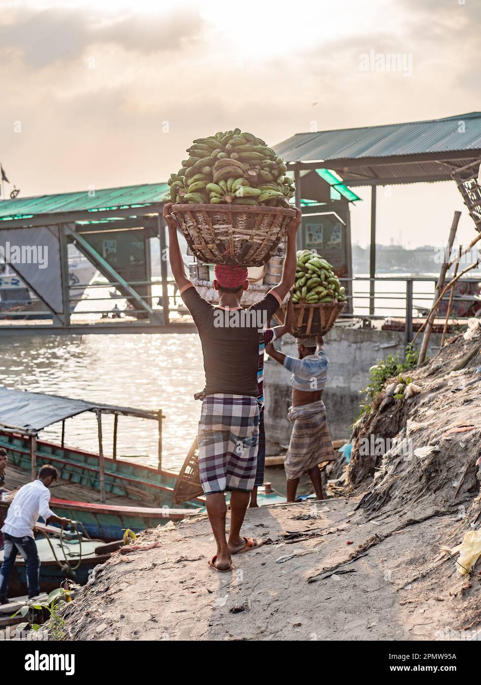 Männer, die grüne Bananen zu den örtlichen Fähren am Wise Ghat Boat Station am Buriganga River in Dhaka, der Hauptstadt von Bangladesch, transportieren. Stockfoto