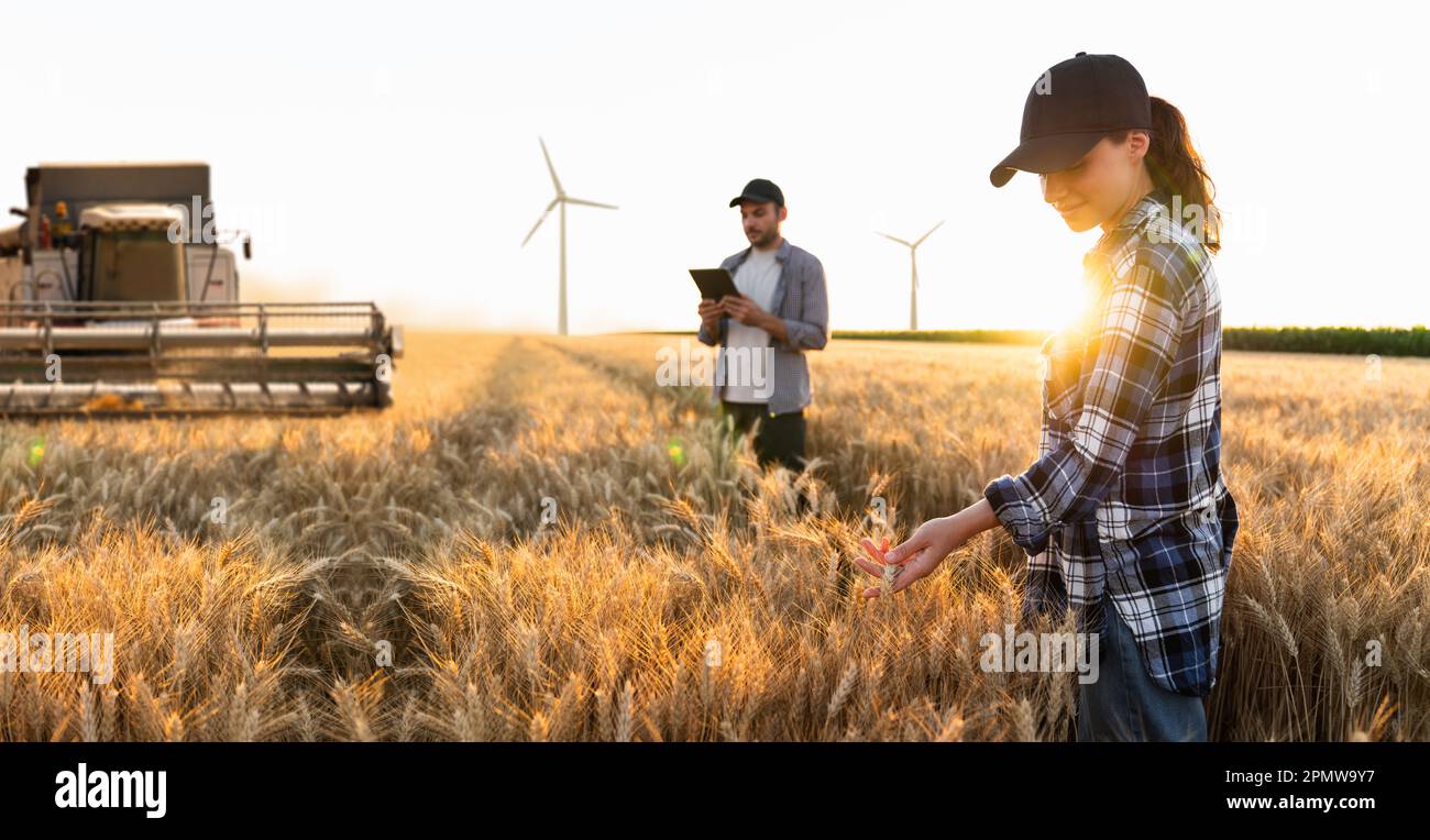 Ein Paar Farmer mit einem digitalen Tablet im Hintergrund der Erntemaschine. Windturbinen am Horizont. Konzept der intelligenten Landwirtschaft. Hochwertiges Foto Stockfoto