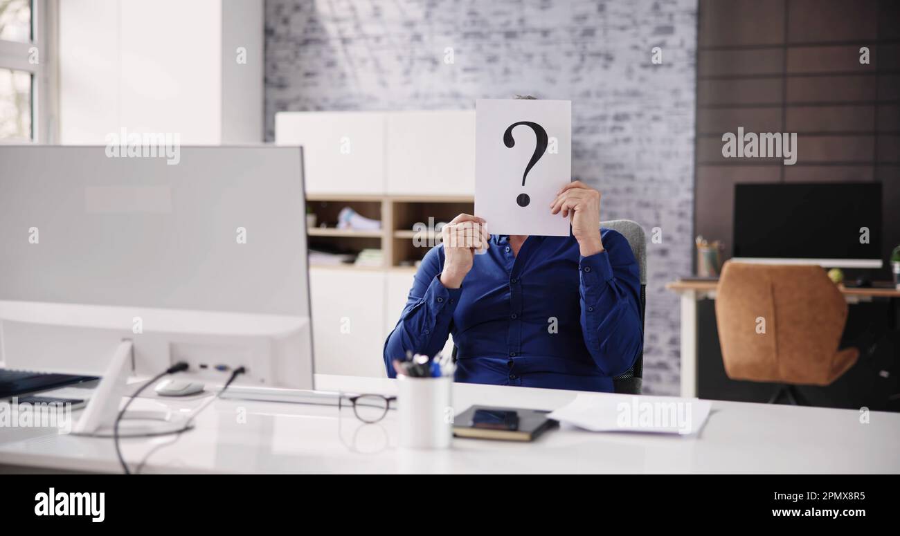 Geschäftsmann Mit Fragezeichen Vor Dem Gesicht Am Schreibtisch Im Büro Stockfoto