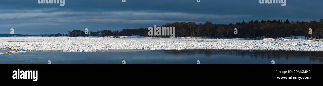 Die stille Schönheit des Winters in Schweden zeigt sich im eisigen Fluss, der einen unheilvollen dunklen Himmel reflektiert, umgeben von einer gefrorenen Landschaft. Stockfoto