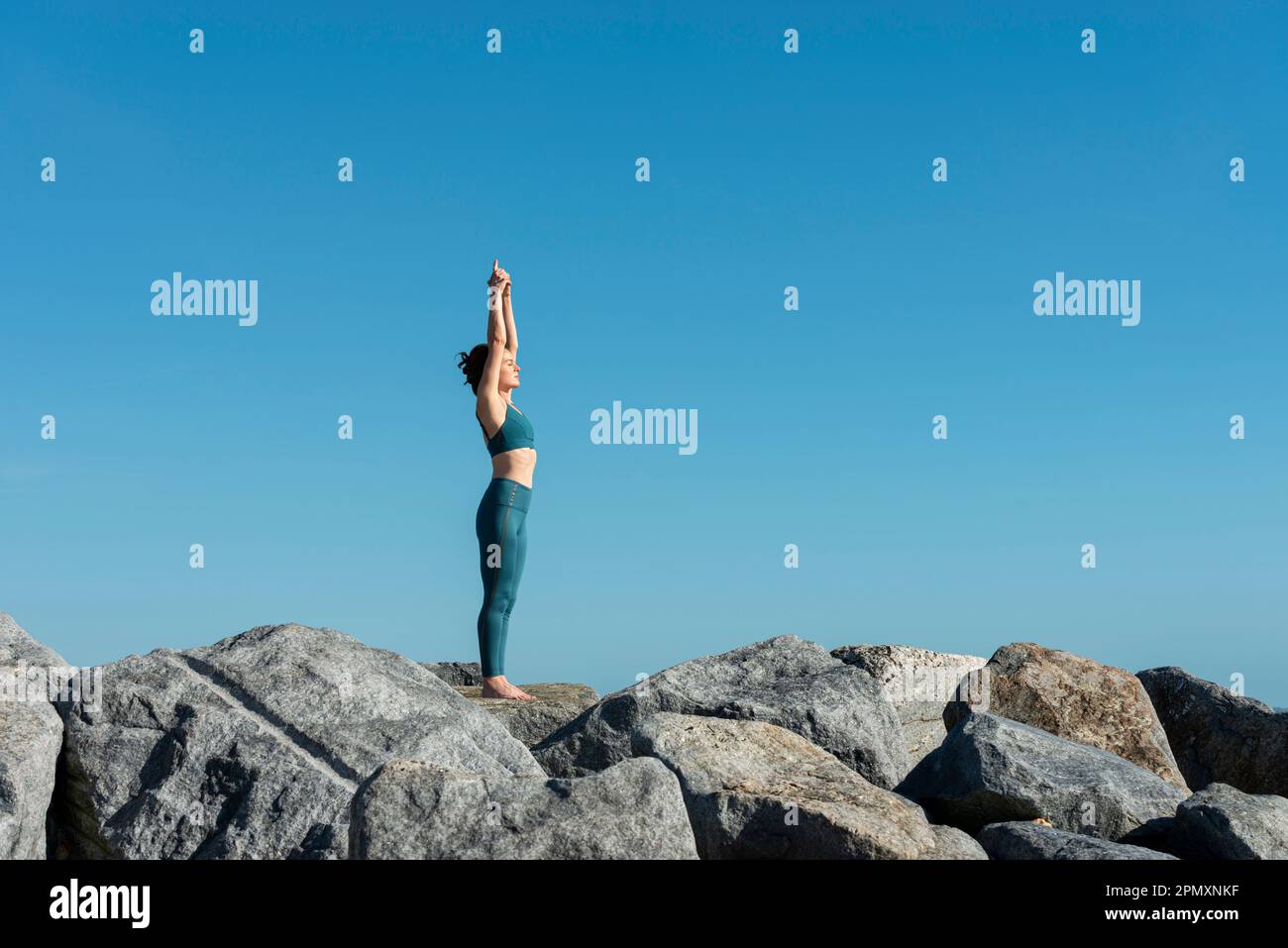 Frau, die sich mit erhobenen Armen streckt, meditiert und draußen Yoga übt. Stockfoto