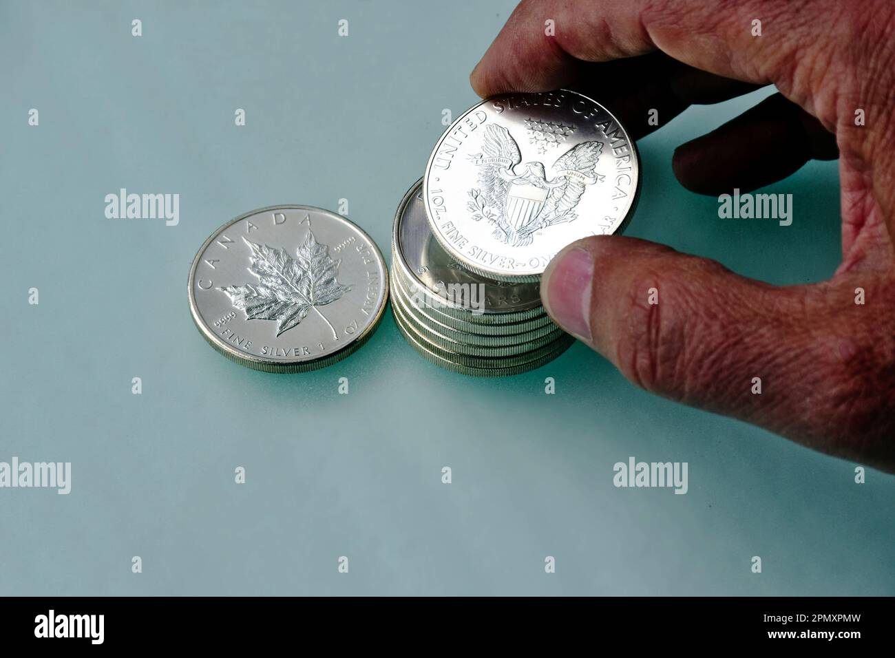 Silbermünzen stapeln. Glänzender 5 Dollar Silberapfel und Adlerstapel. Körnige dunkelgraue Glasoberfläche. Kostensparendes Konzept. Finger halten fünf Dollar Stockfoto
