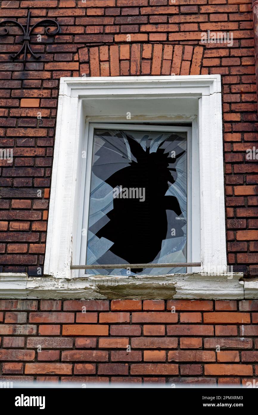 Zerbrochenes Fenster mit weißem Rahmen in einer Ziegelwand Stockfoto