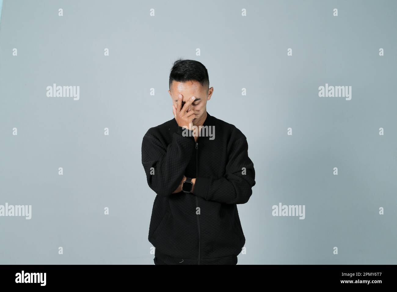 Ein junger Mann, der ein schwarzes Hemd trägt, beklagt seine Angst, isoliert auf grauem Hintergrund Stockfoto