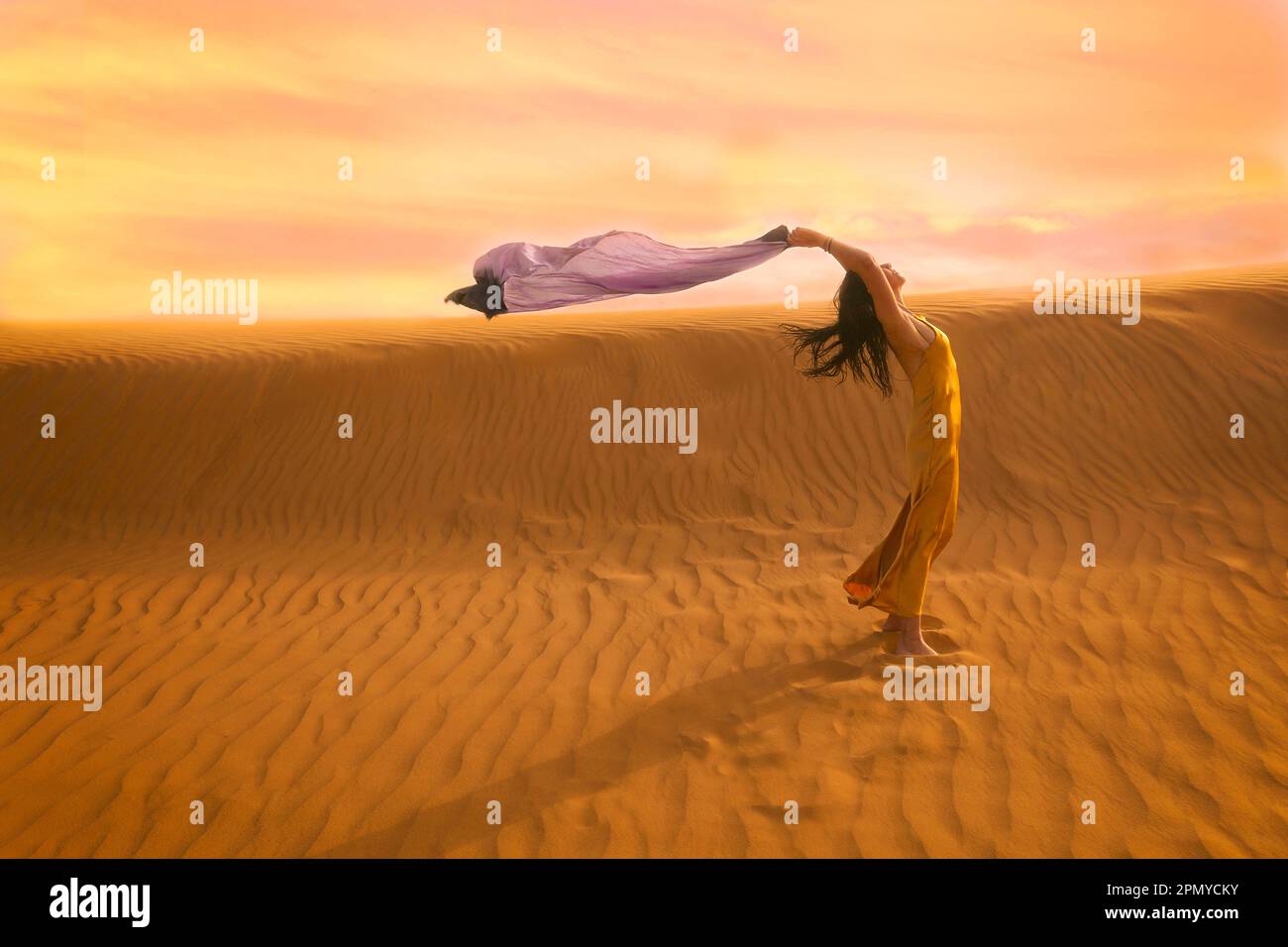 Eine Frau in gelbem Kleid, die mit dem Wind in der Wüste V spielt Stockfoto