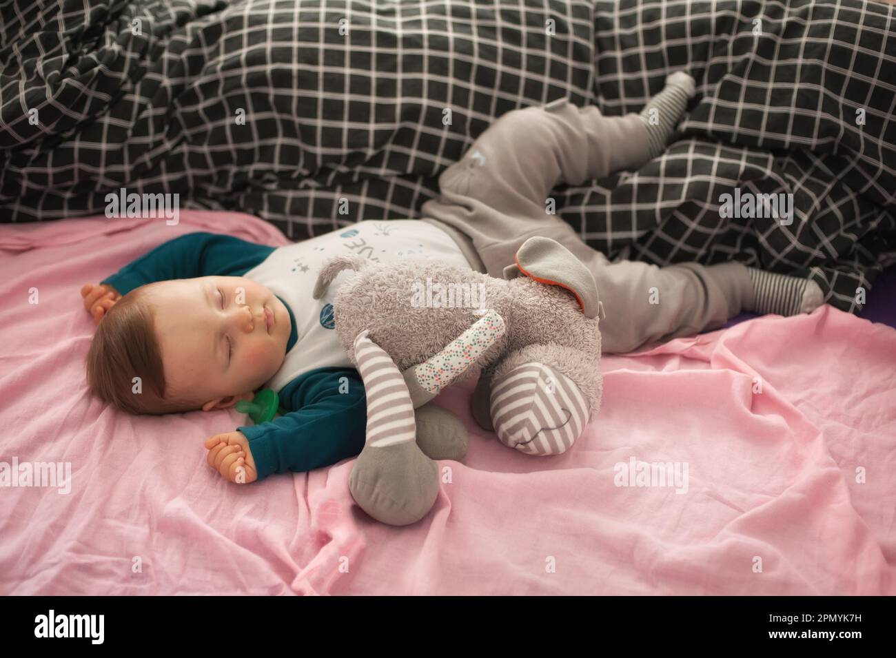 Ein süßer kleiner Junge schläft friedlich und entspannt auf seinem Bett mit Spielzeug. Draufsicht des Kinderbetts. Liebe und Familiengefühle Stockfoto